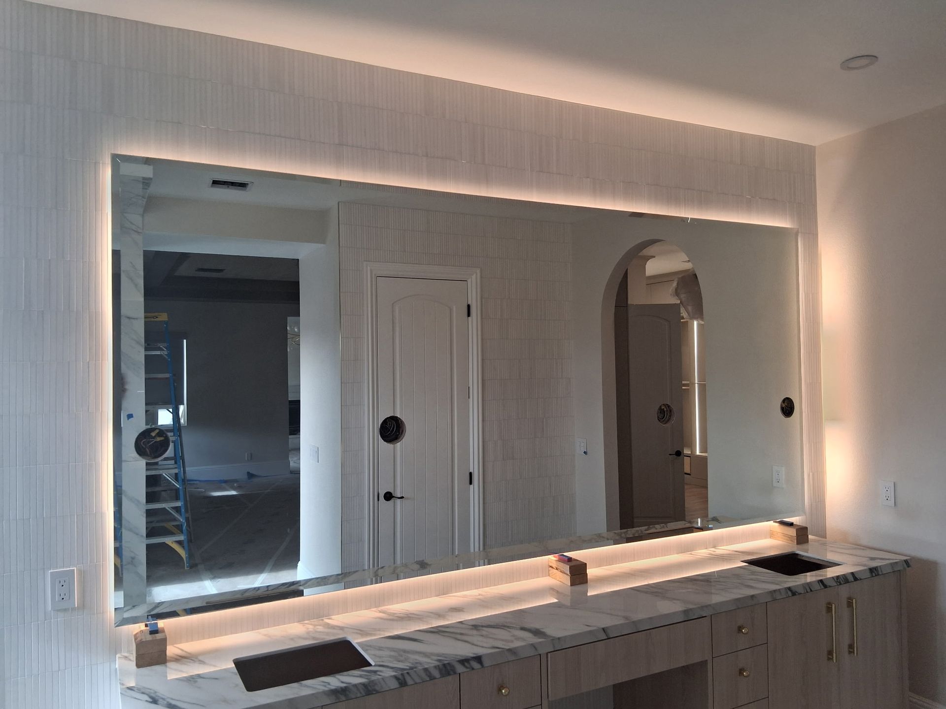 Large bathroom vanity with lit mirror, marble countertop, and wall sconces in a modern interior
