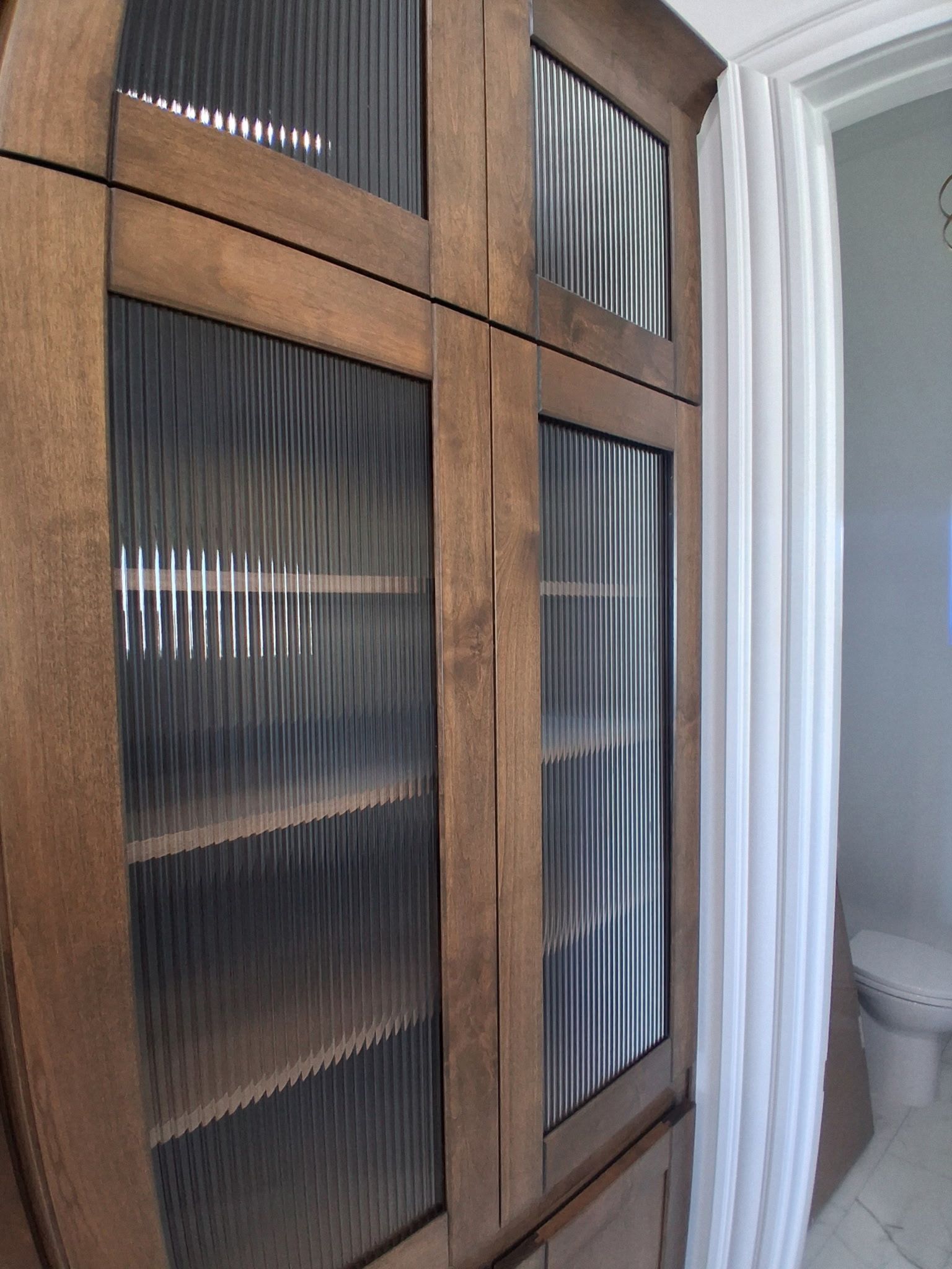 Wooden cabinet with textured glass doors beside a white shower curtain in a bathroom