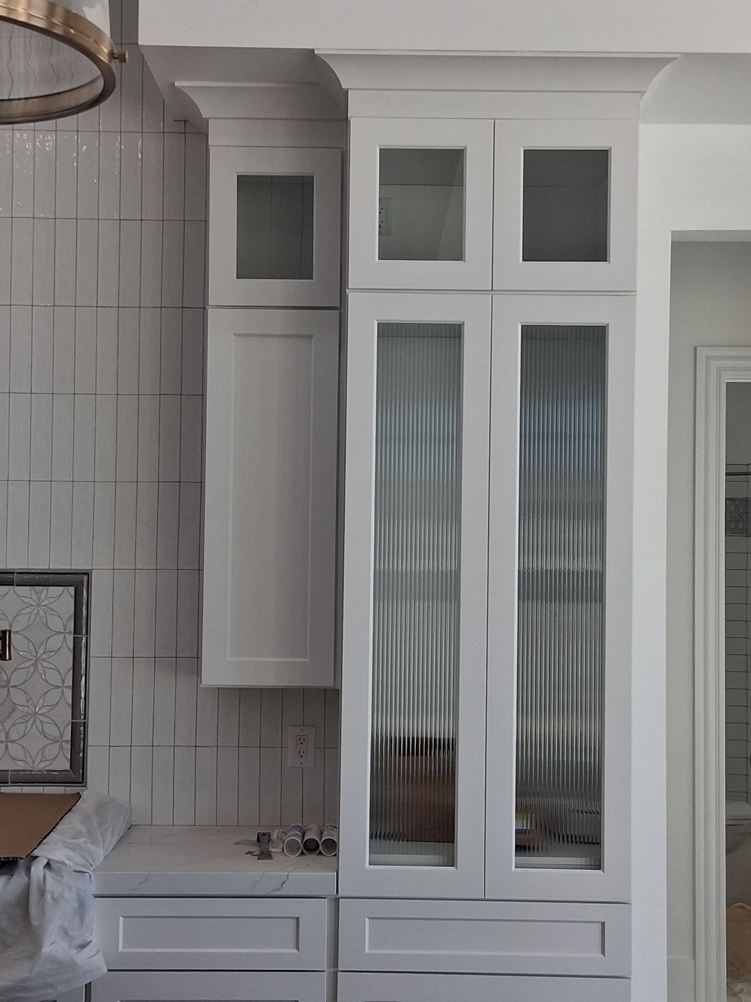 White kitchen cabinets with glass doors and tiled backsplash on the left edge