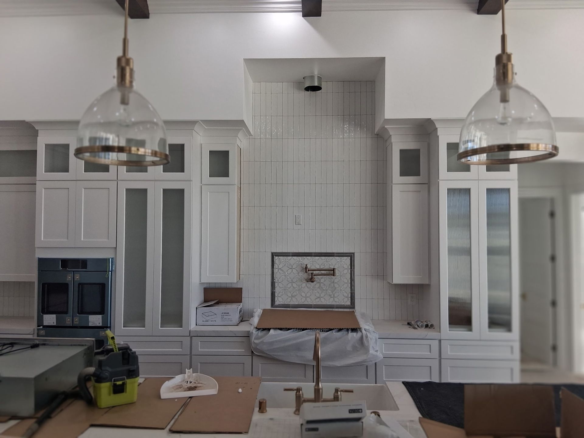 Modern white kitchen with glass pendant lights, gray tile backsplash, and a central island under renovation