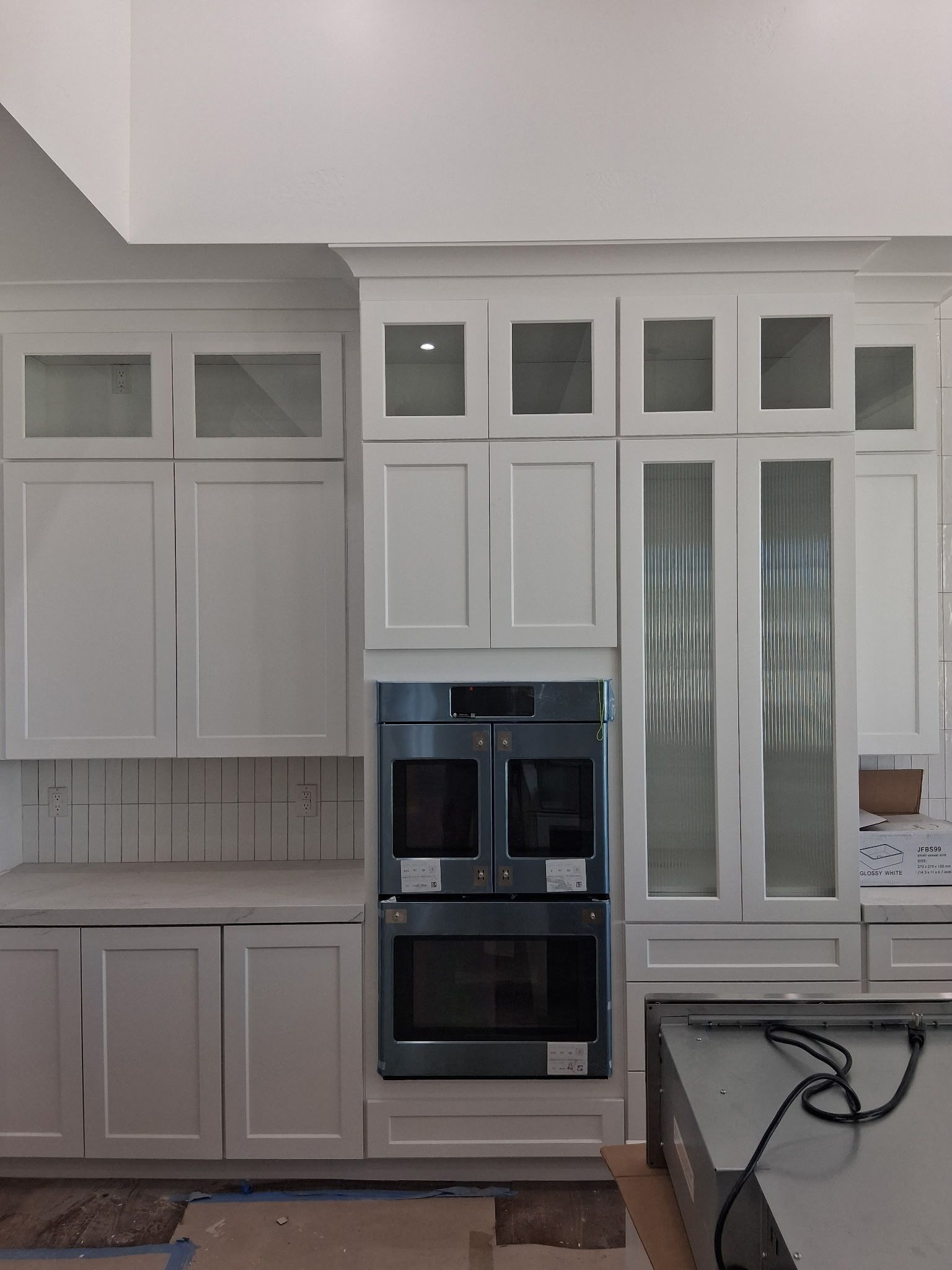 Bright white kitchen with built-in oven, cabinets, glass doors, and a countertop with a cord.