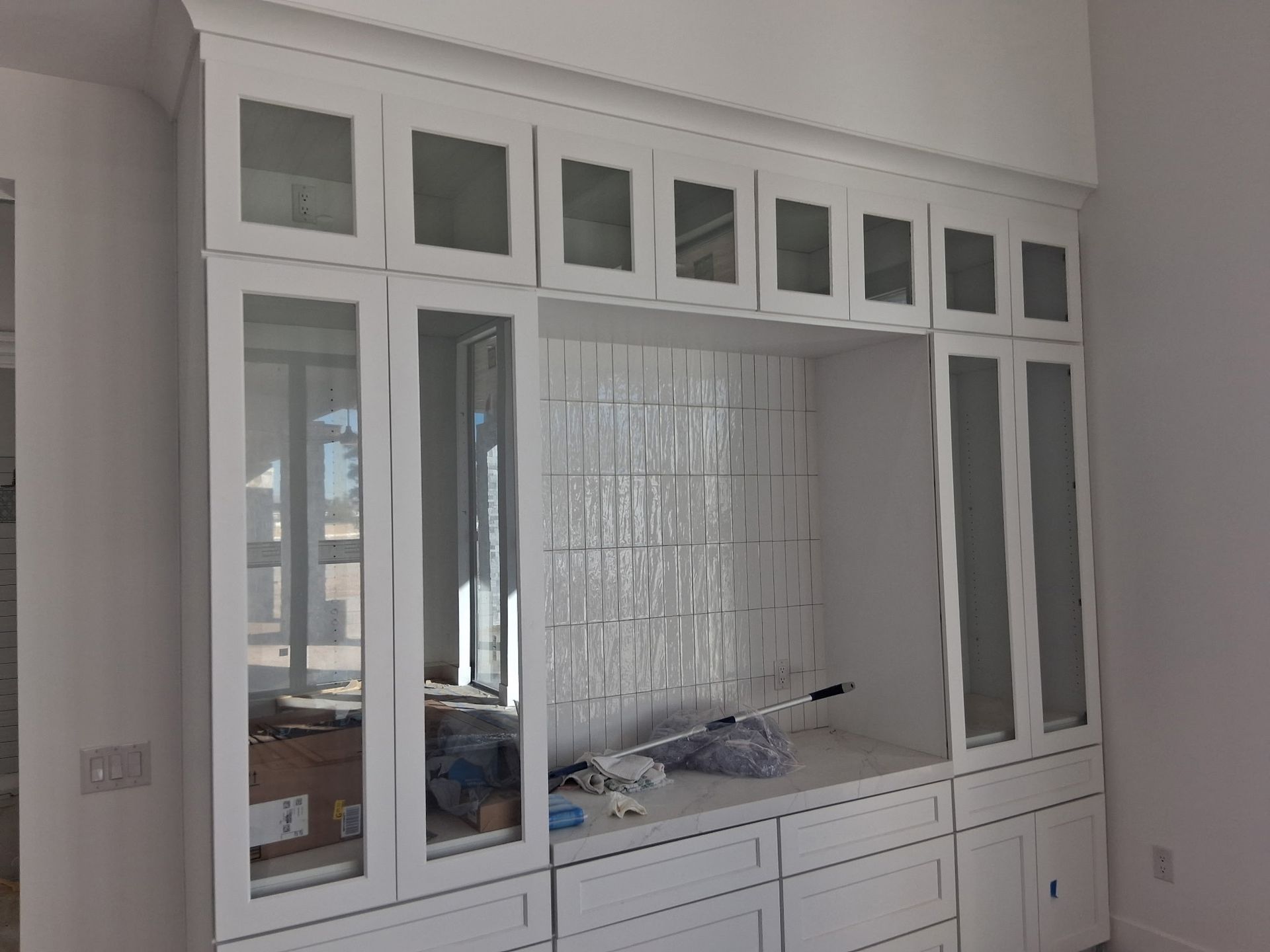 White built-in wall cabinet with glass panels and drawers in a room under renovation