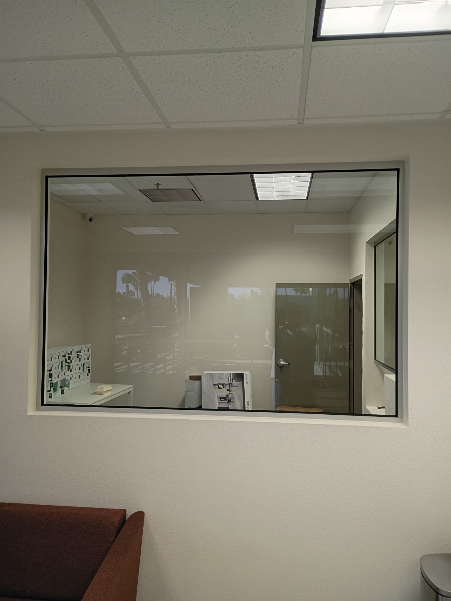 Interior office view through a large window into a small room with a deskP and door.