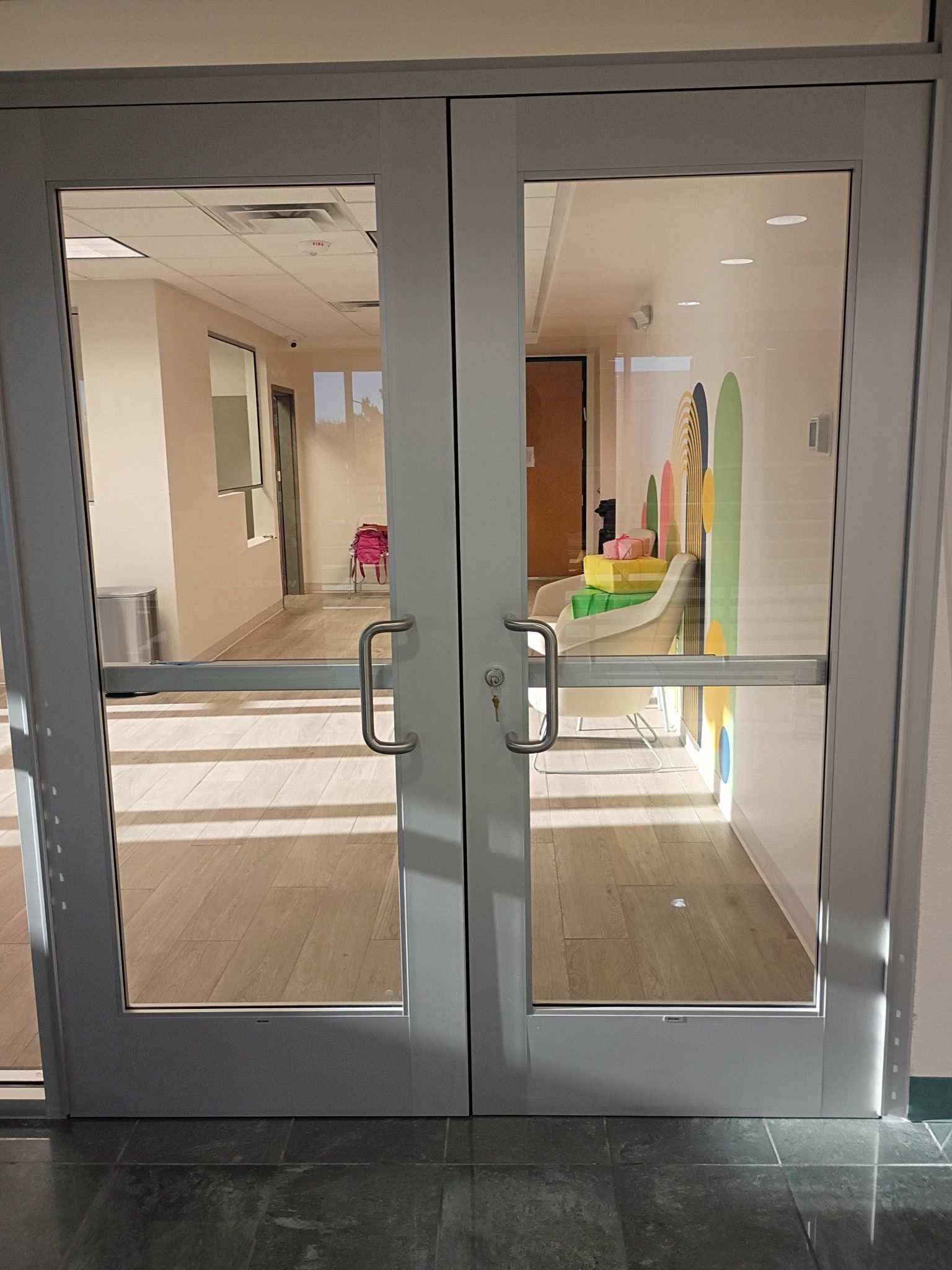Glass double doors at a building entrance, with a bright lobby and colorful display visible inside.