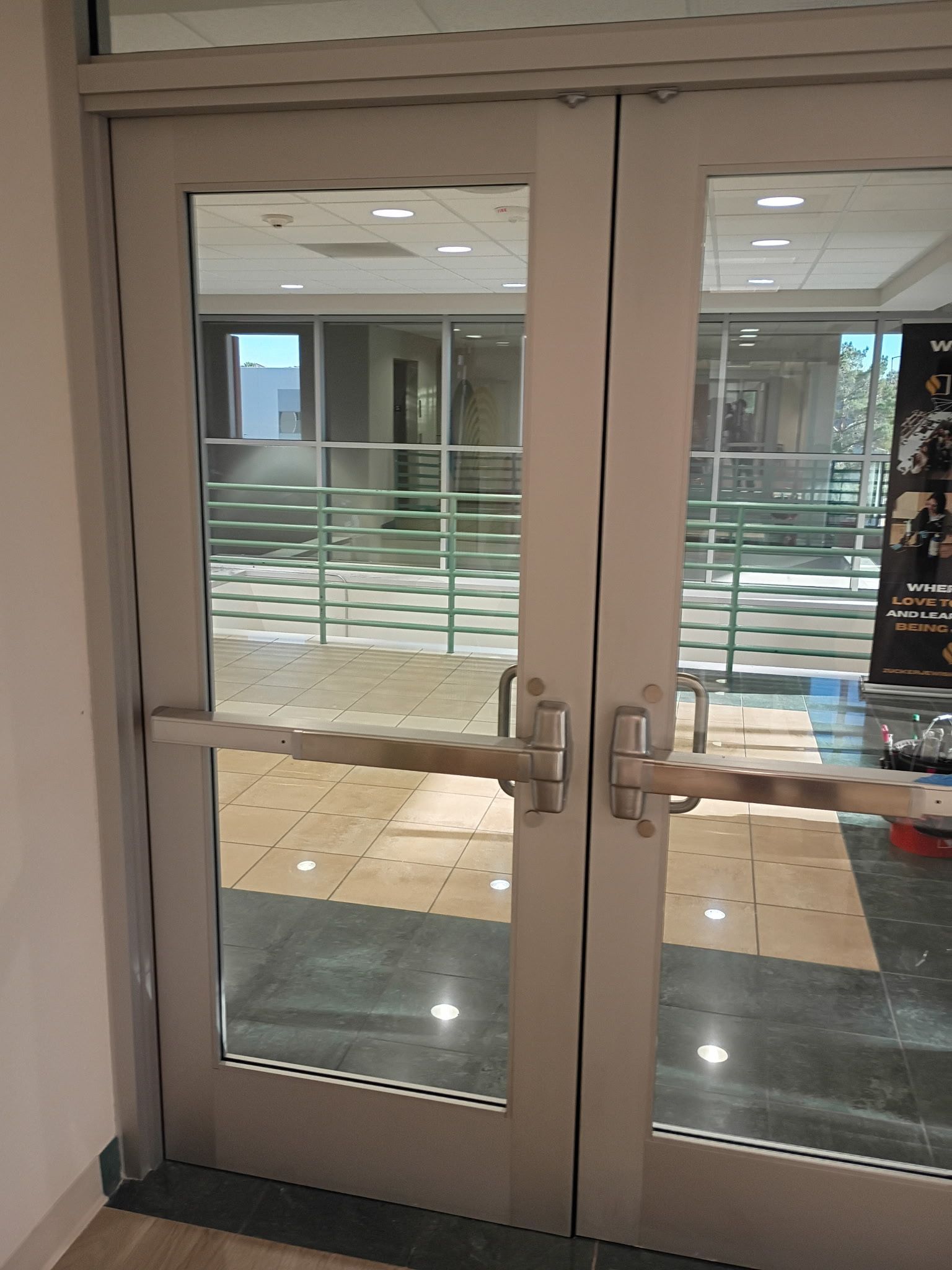 Glass double doors with metal handles in a hallway entrance, leading to a bright lobby outside