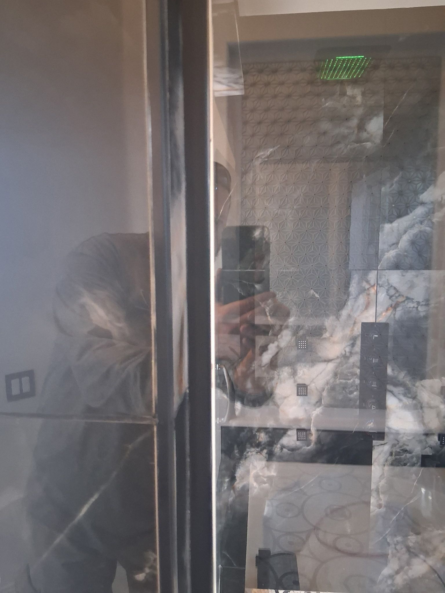 Person behind a glass partition in a dim room, with reflections and a green light above.