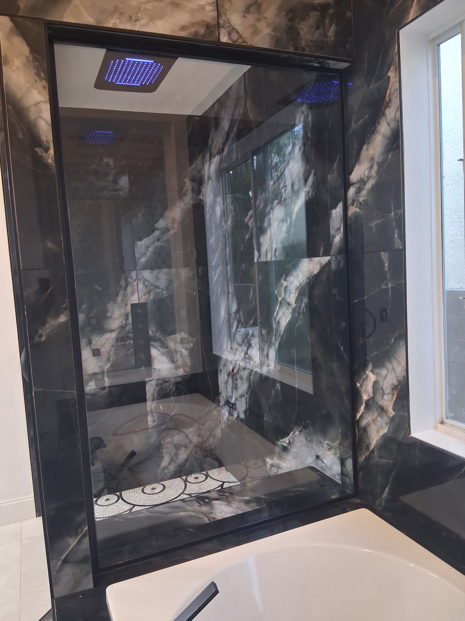 Empty black shower stall with stained walls, shelf, and a window beside a bathtub.