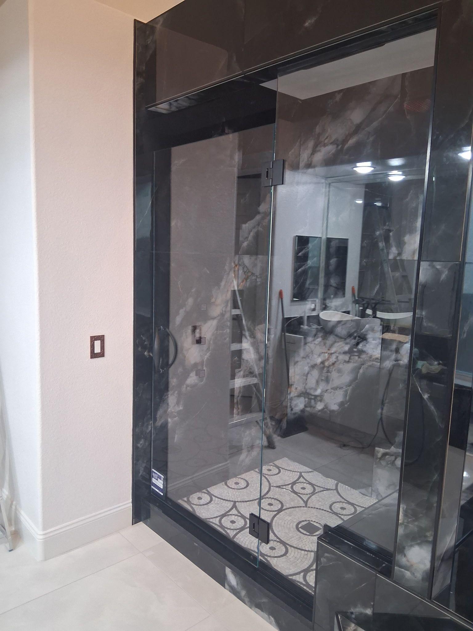 Damaged black-framed glass shower enclosure in a bathroom, with broken panels and debris on the floor