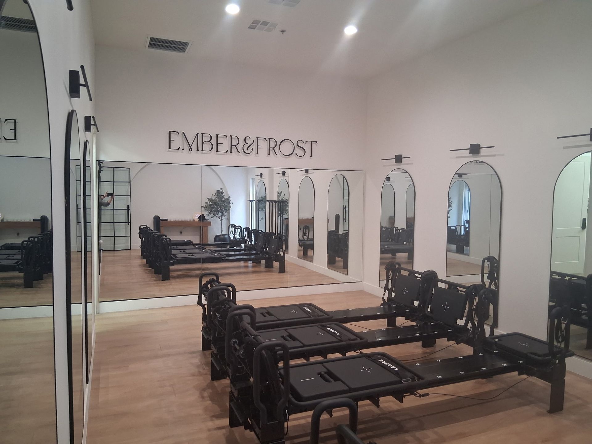 Pilates studio with reformer machines, mirrored wall, and “EMBODI POST” sign