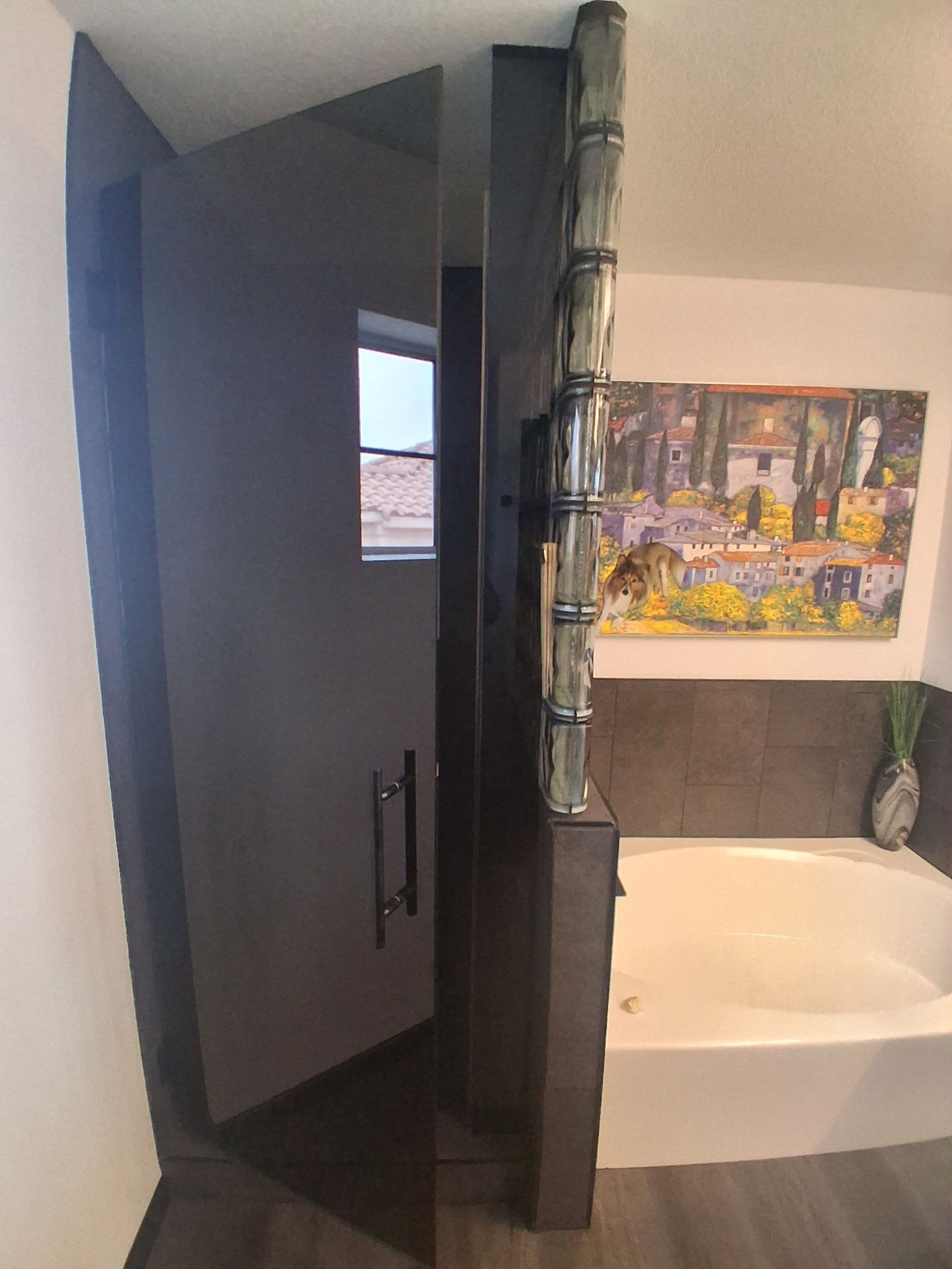 Bathroom with dark cabinet door, bathtub, wall art, and a vase on a shelf.