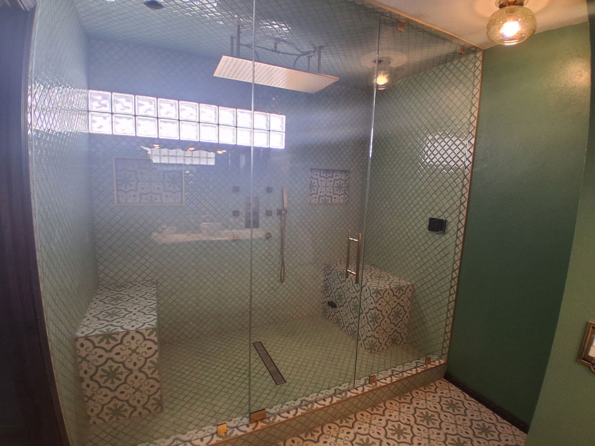 Glass shower stall with patterned tiles, green wall, and hanging lights in a bathroom