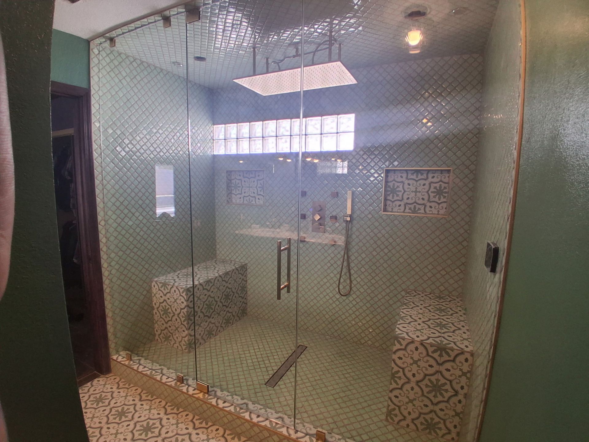 Glass shower stall with patterned stools, a floor drain, and frosted window light in a tiled bathroom
