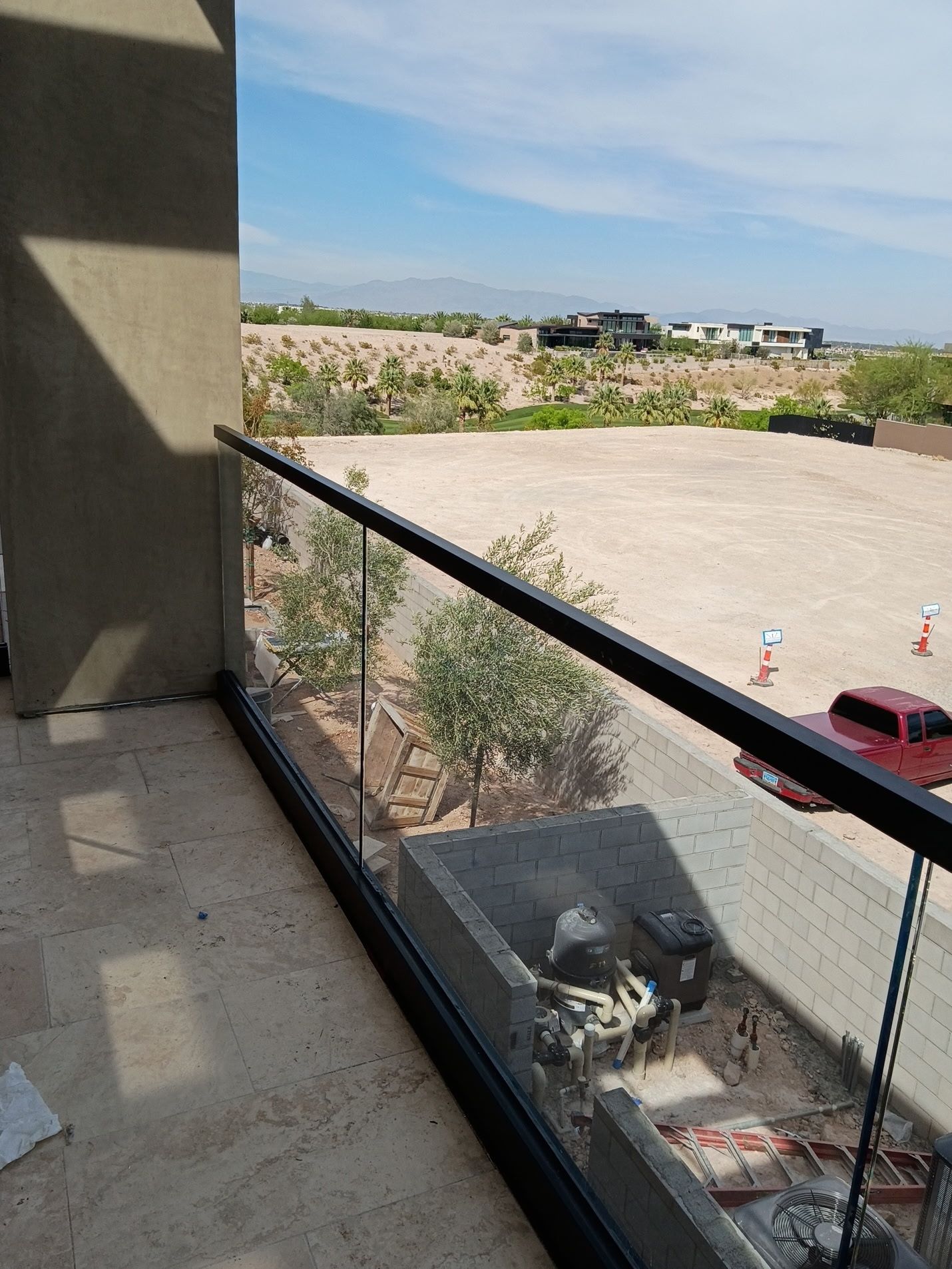 Balcony with glass railing overlooking a parking lot, desert landscaping, and distant mountains under a blue sky