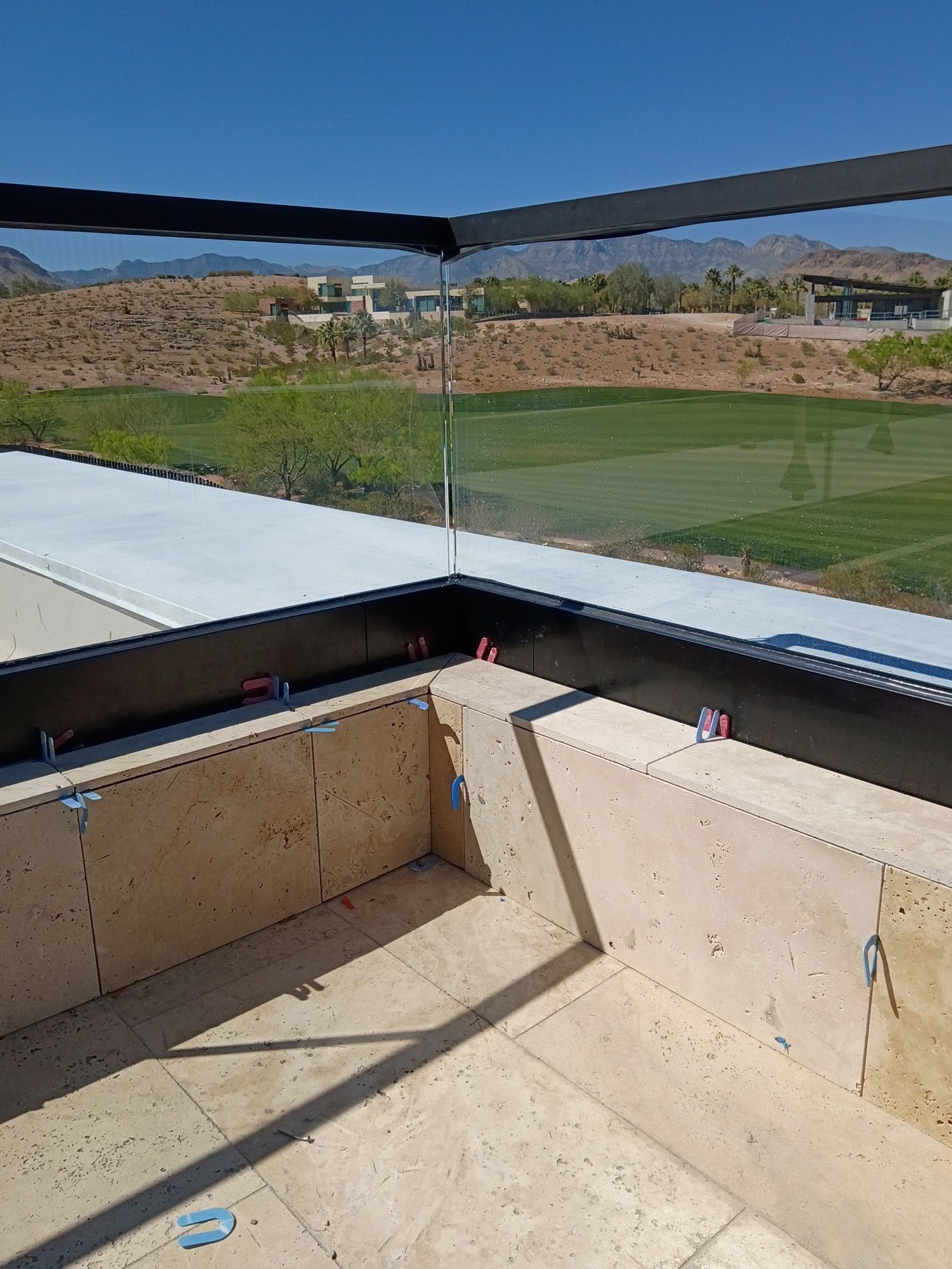 Balcony or rooftop patio with glass railing overlooking a grassy field and hills under a clear sky
