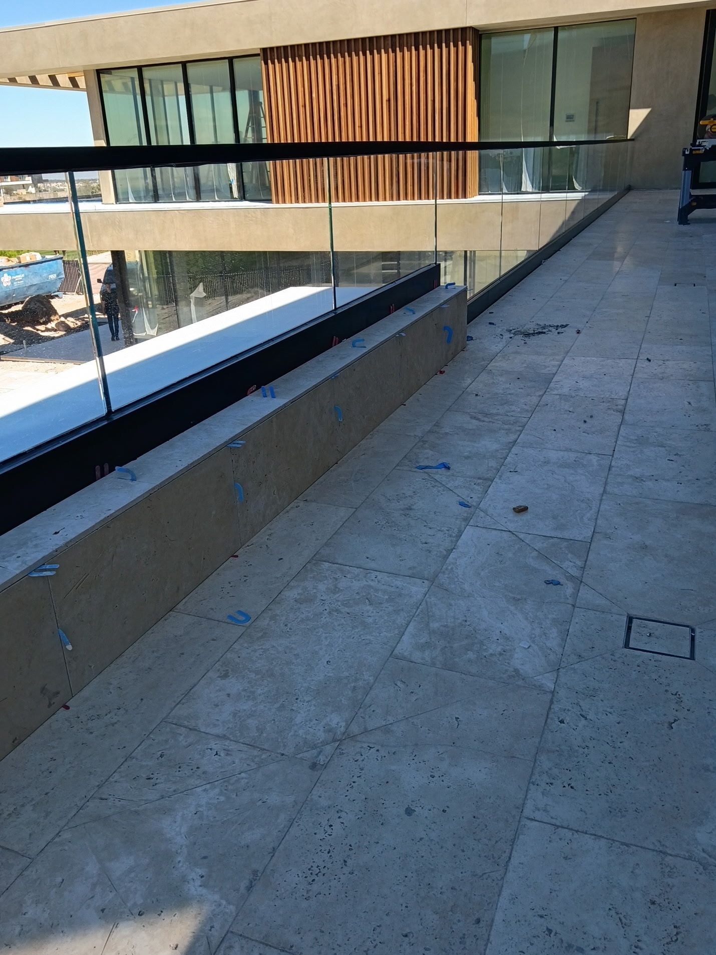 Modern balcony walkway with glass railing and stone floor beside a building