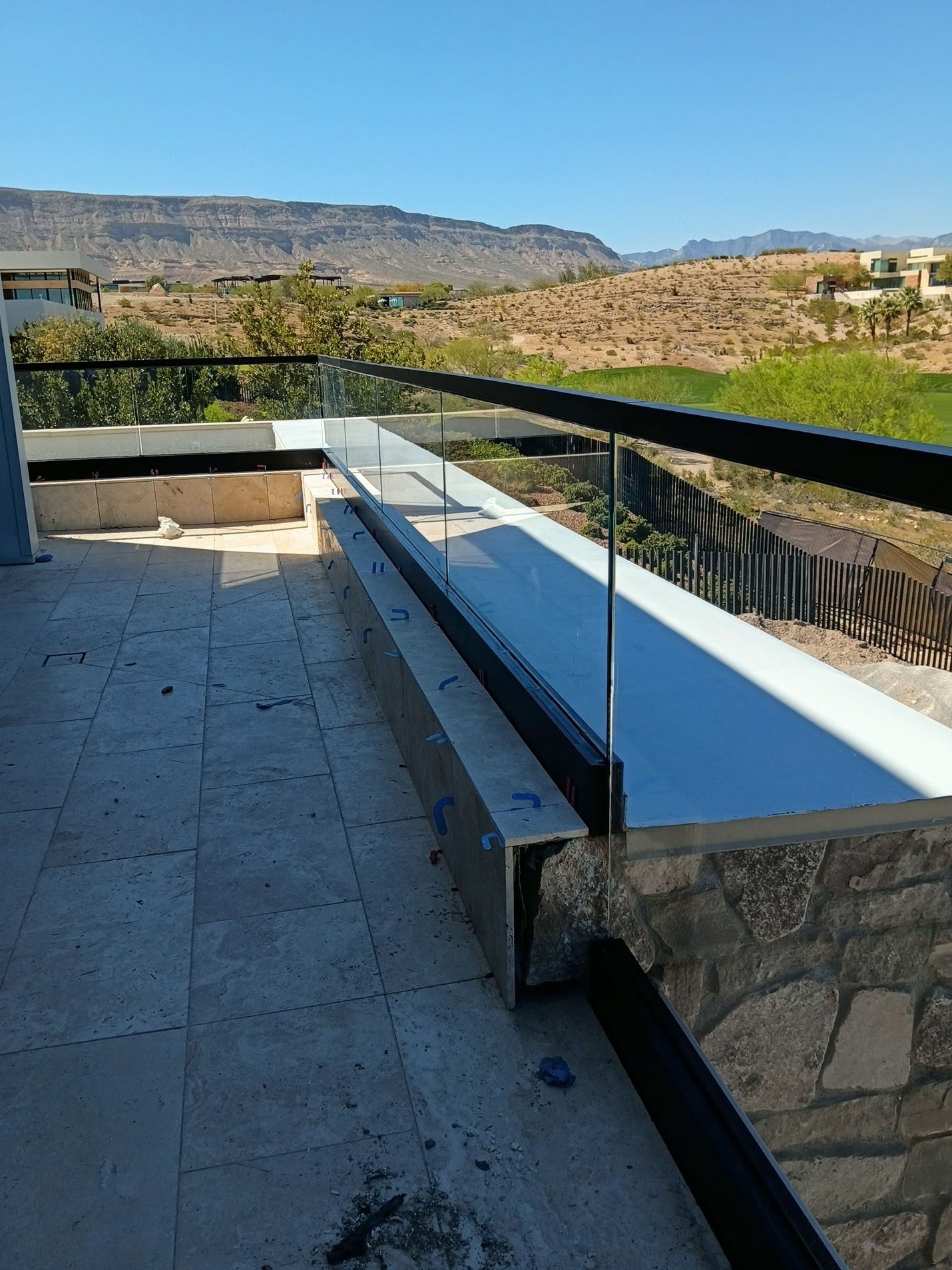 Modern outdoor patio with stone seating, glass railing, and mountain view