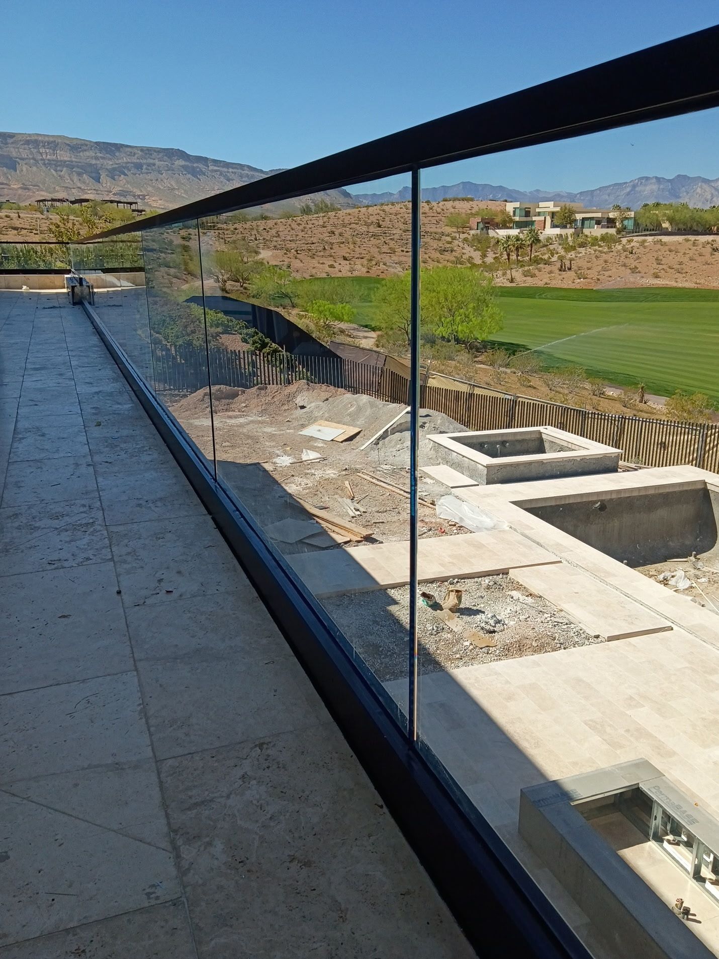 Modern outdoor walkway with glass railing overlooking a landscaped construction site and distant hills