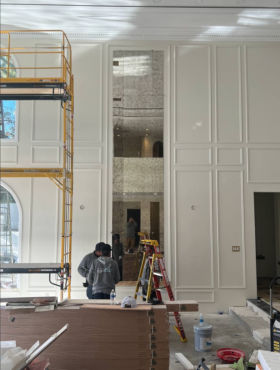 Interior construction site with scaffolding, white paneled walls, and workers installing a tall opening