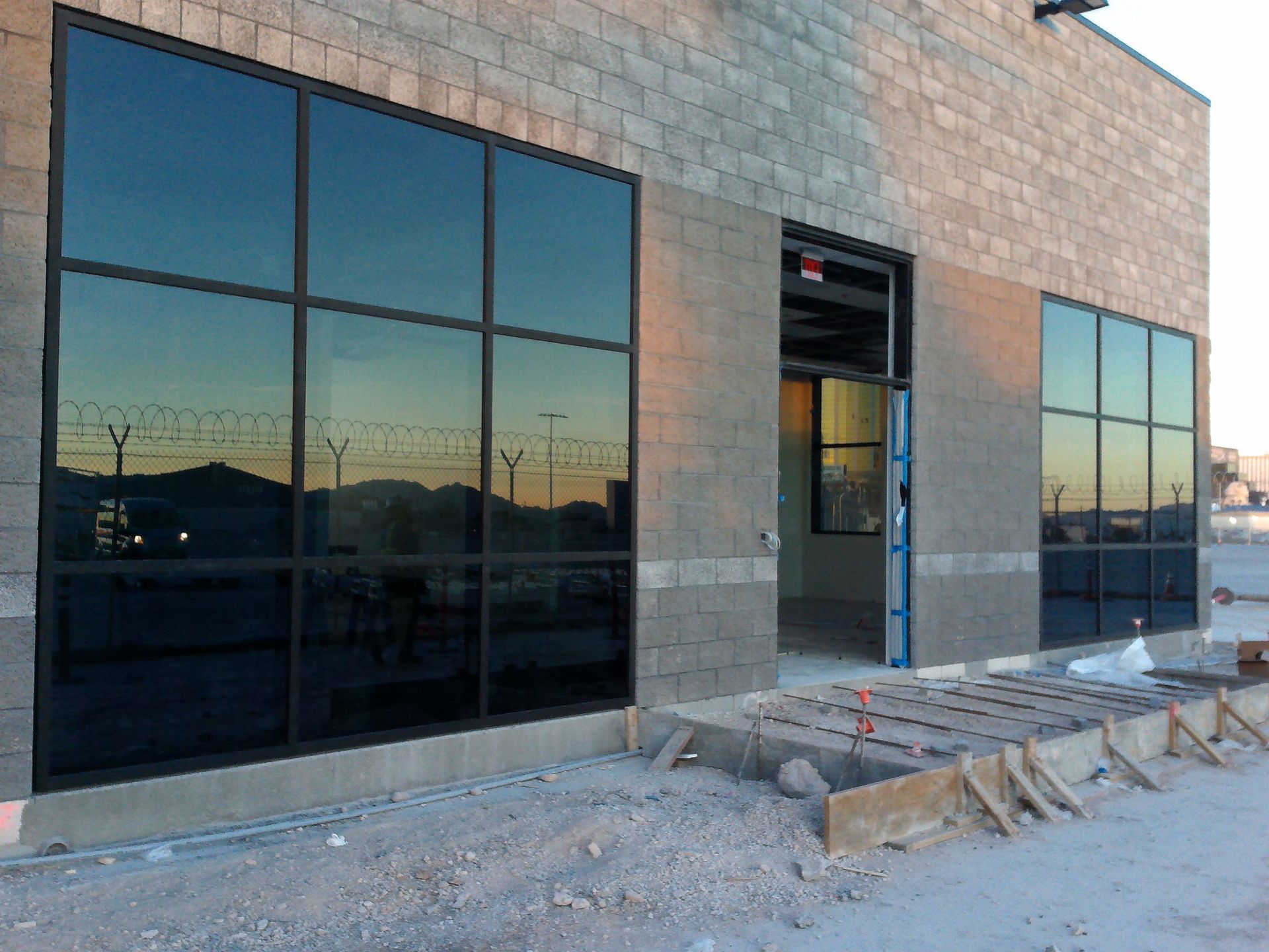 Storefront with large dark windows and an unfinished entrance beside a gravel construction area