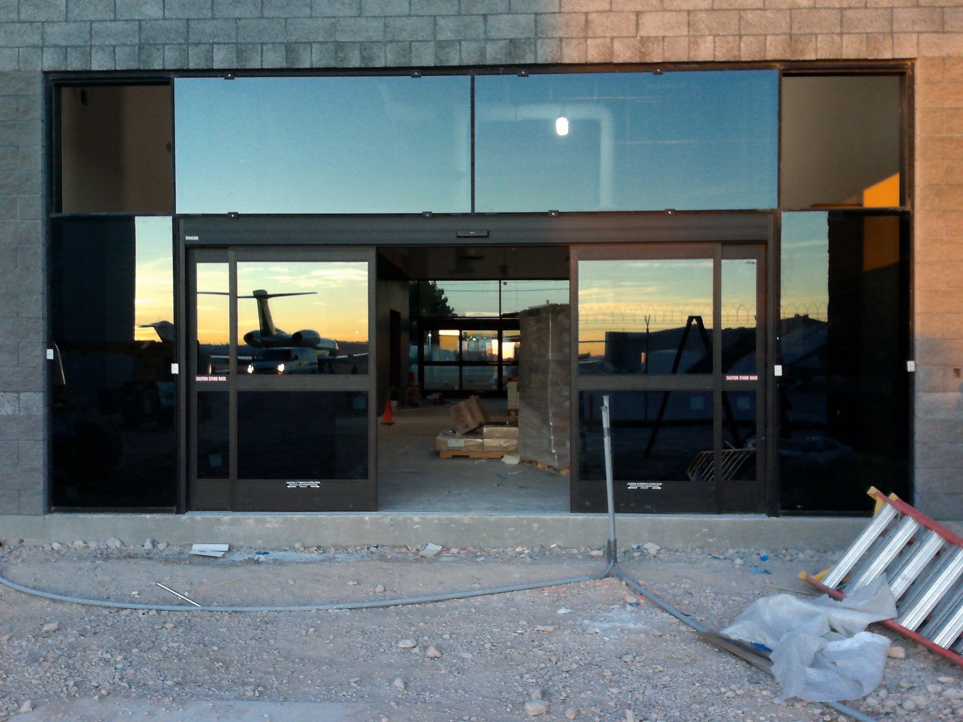 Glass-front commercial building under construction with open entrance and debris in front