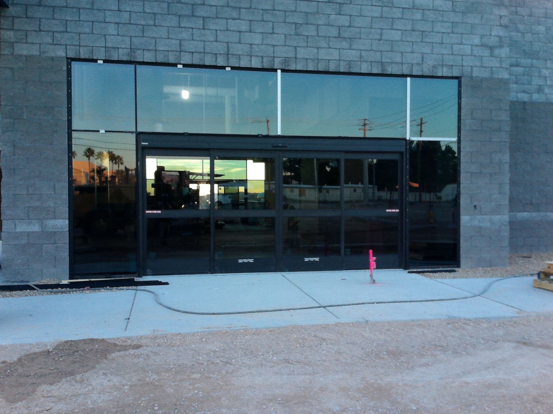 Glass storefront with dark doors set in a gray brick wall, reflected by the street outside.