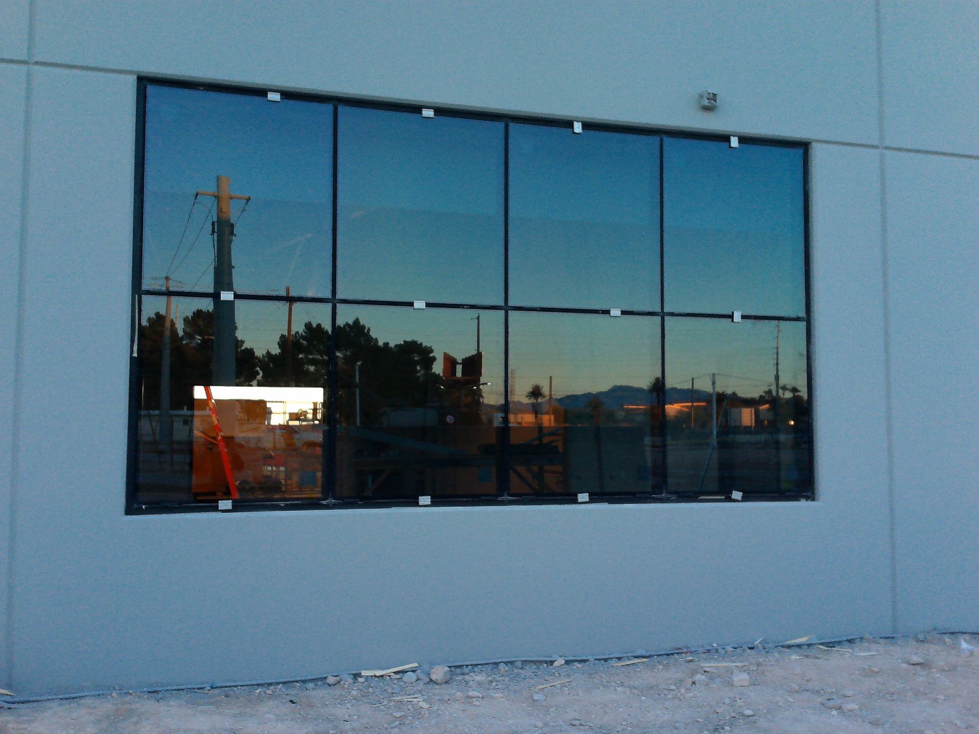 Blue building wall with a large reflective window showing a sunset and nearby structures