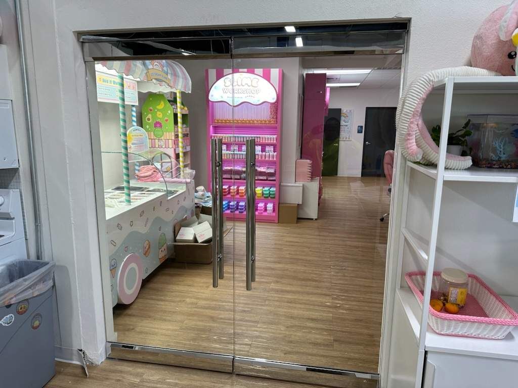 Shop entrance with glass sliding doors, pastel display shelves, and a bright pink arcade machine inside.