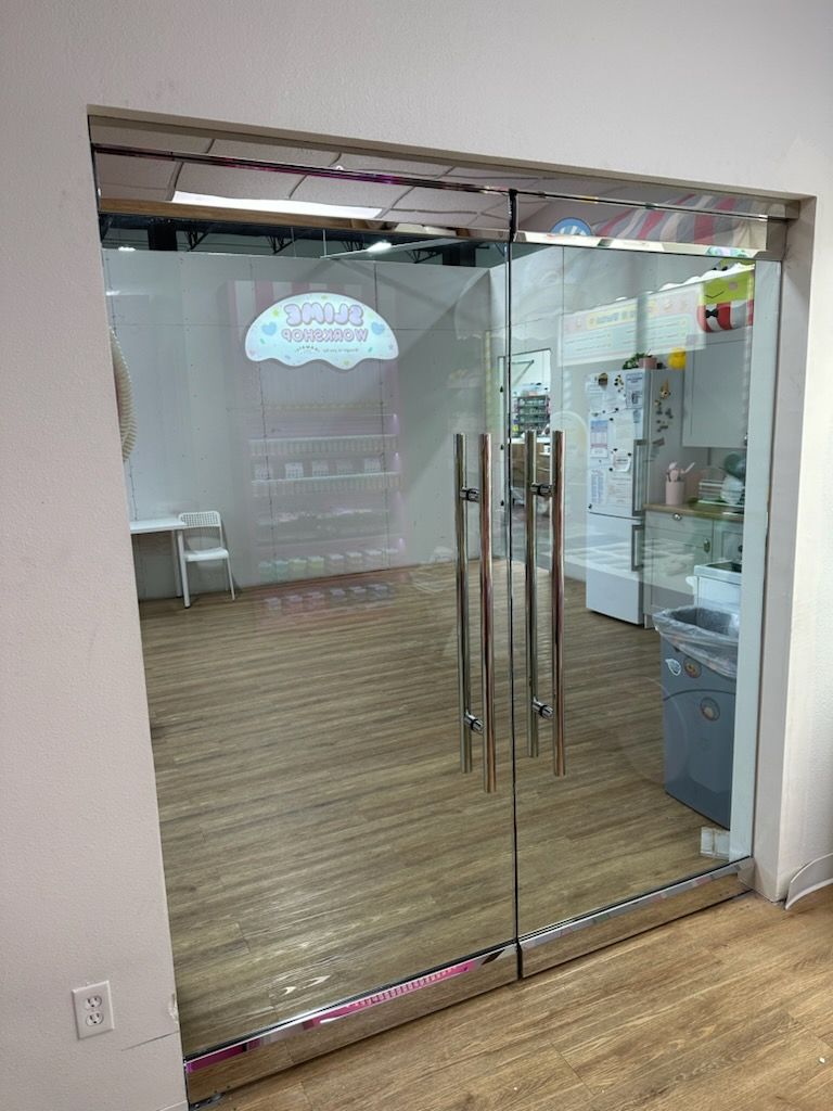 Glass double doors leading to a small office lobby with wood flooring and a chair inside.