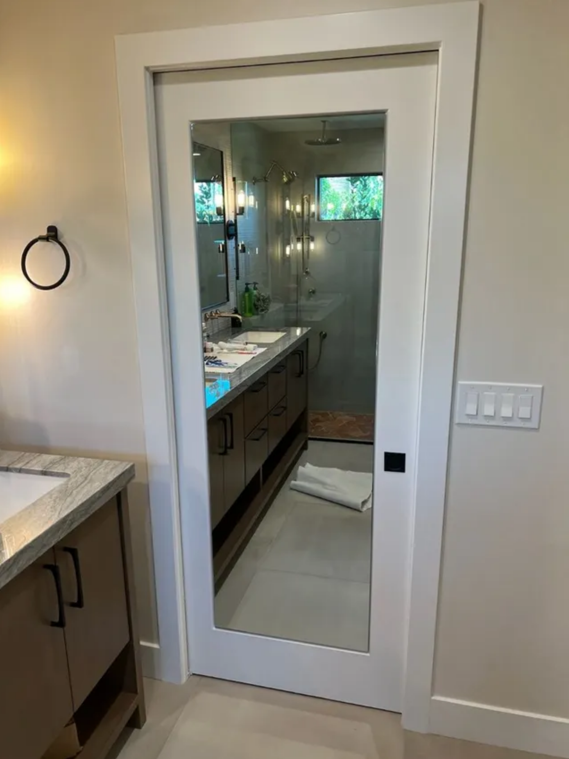 Bathroom doorway with white-framed glass door, vanity visible inside, and wall sconce on the left.