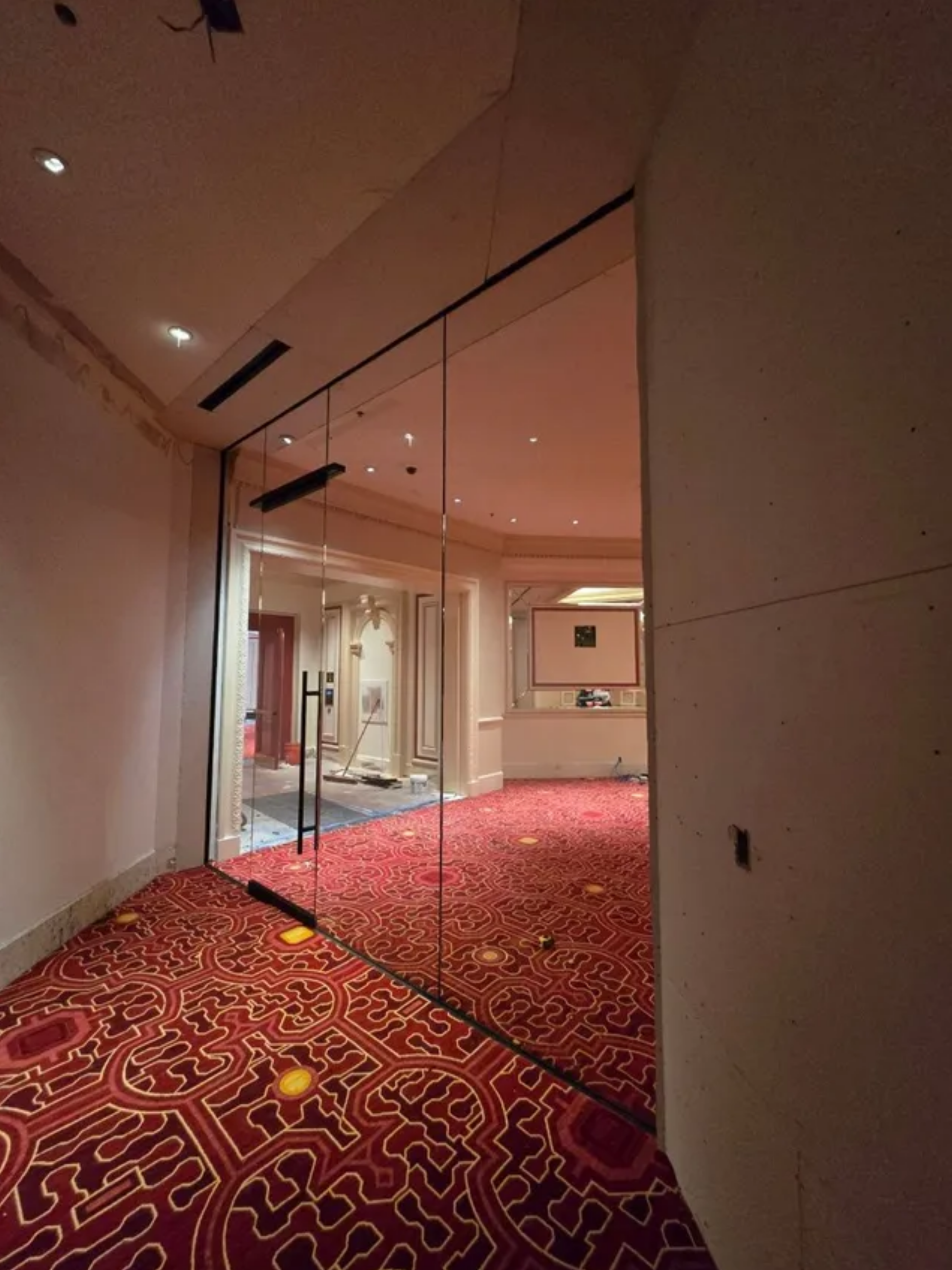 Empty hallway with red patterned carpet and glass walls under soft ceiling lights