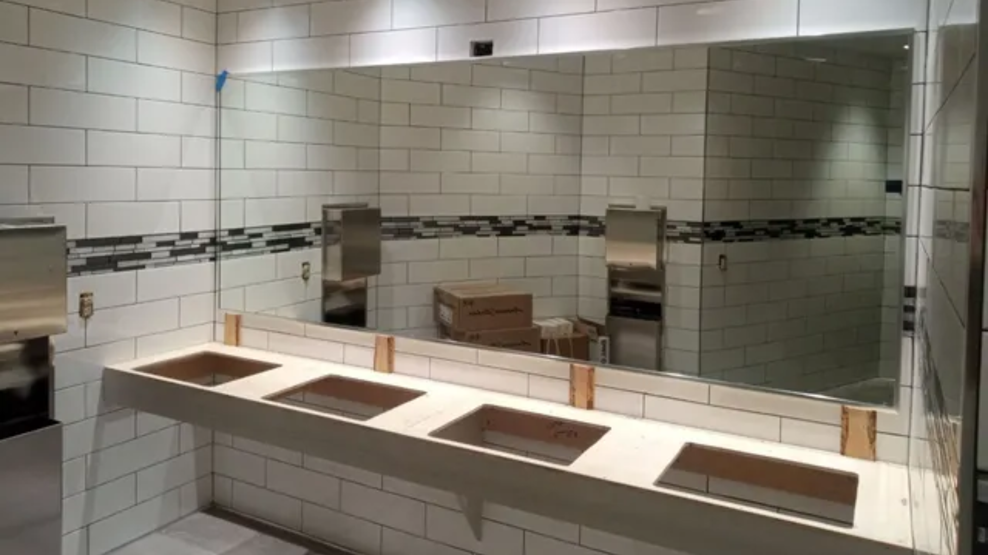 White-tiled restroom with a large mirror and a row of empty sinks on a countertop