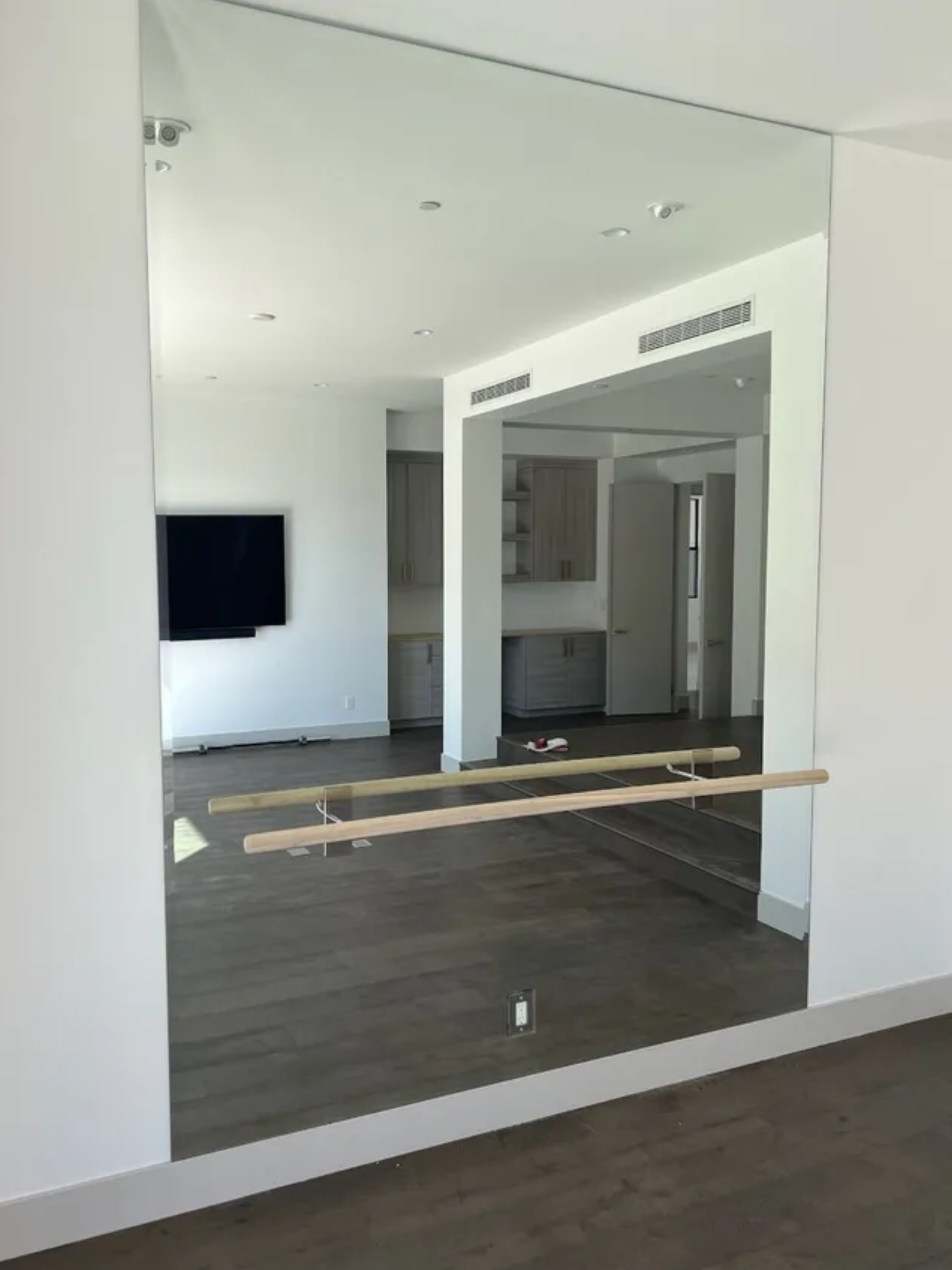 Living room with large wall mirror, dark floors, white walls, and a TV mounted on the left.