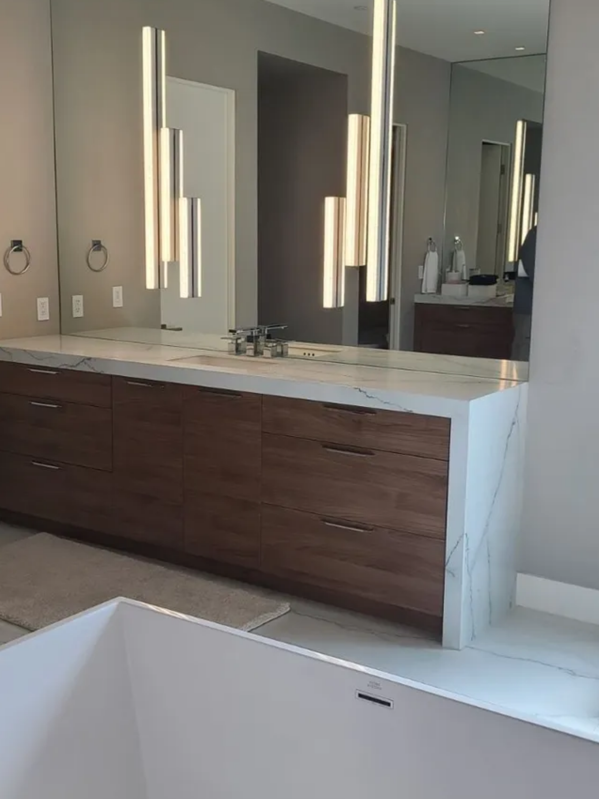 Modern bathroom with double vanity, large mirrors, vertical lights, and a freestanding tub
