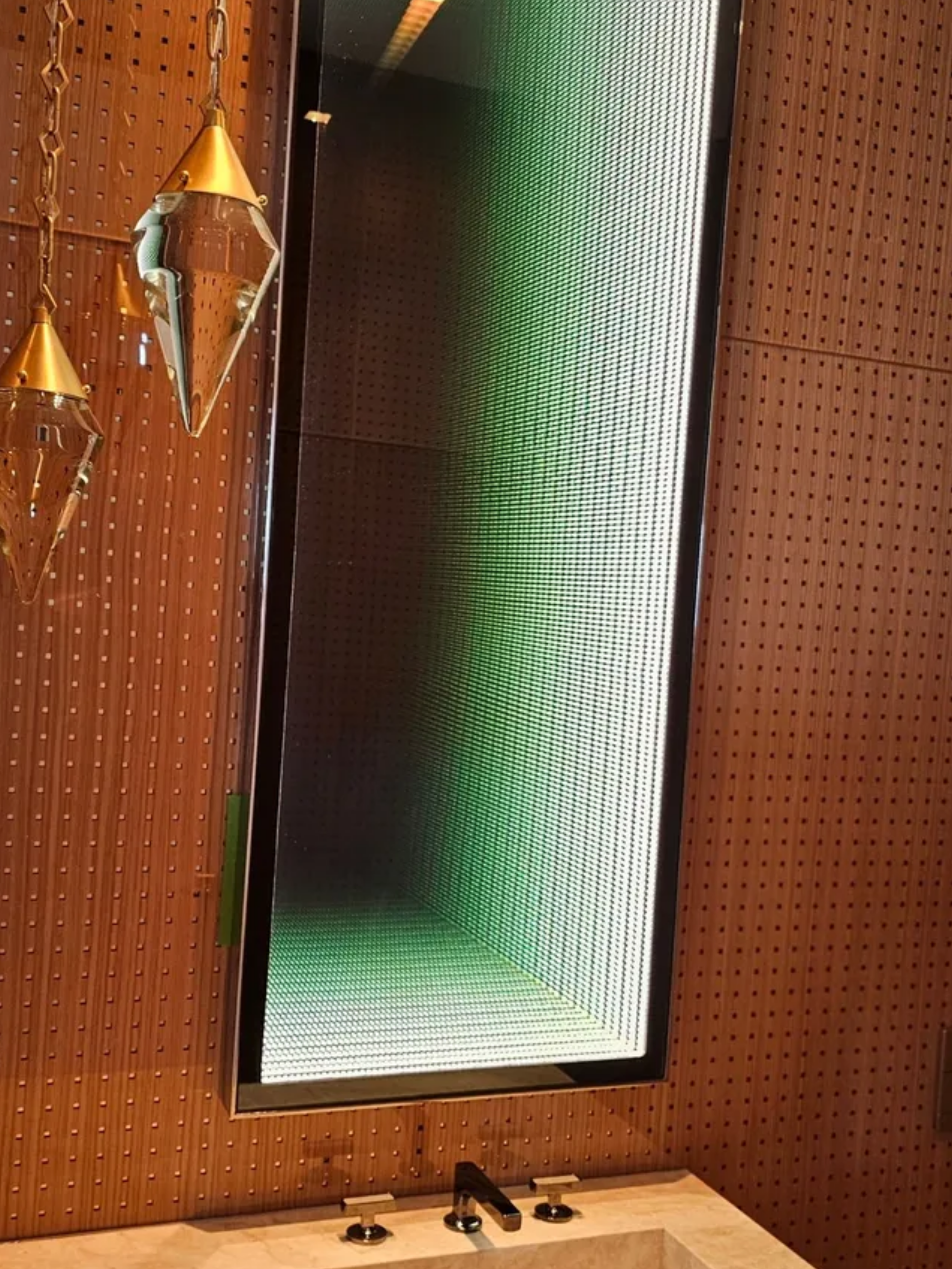 Bathroom with a lit mirror, green glow, wooden wall, and hanging pendant lights above a sink