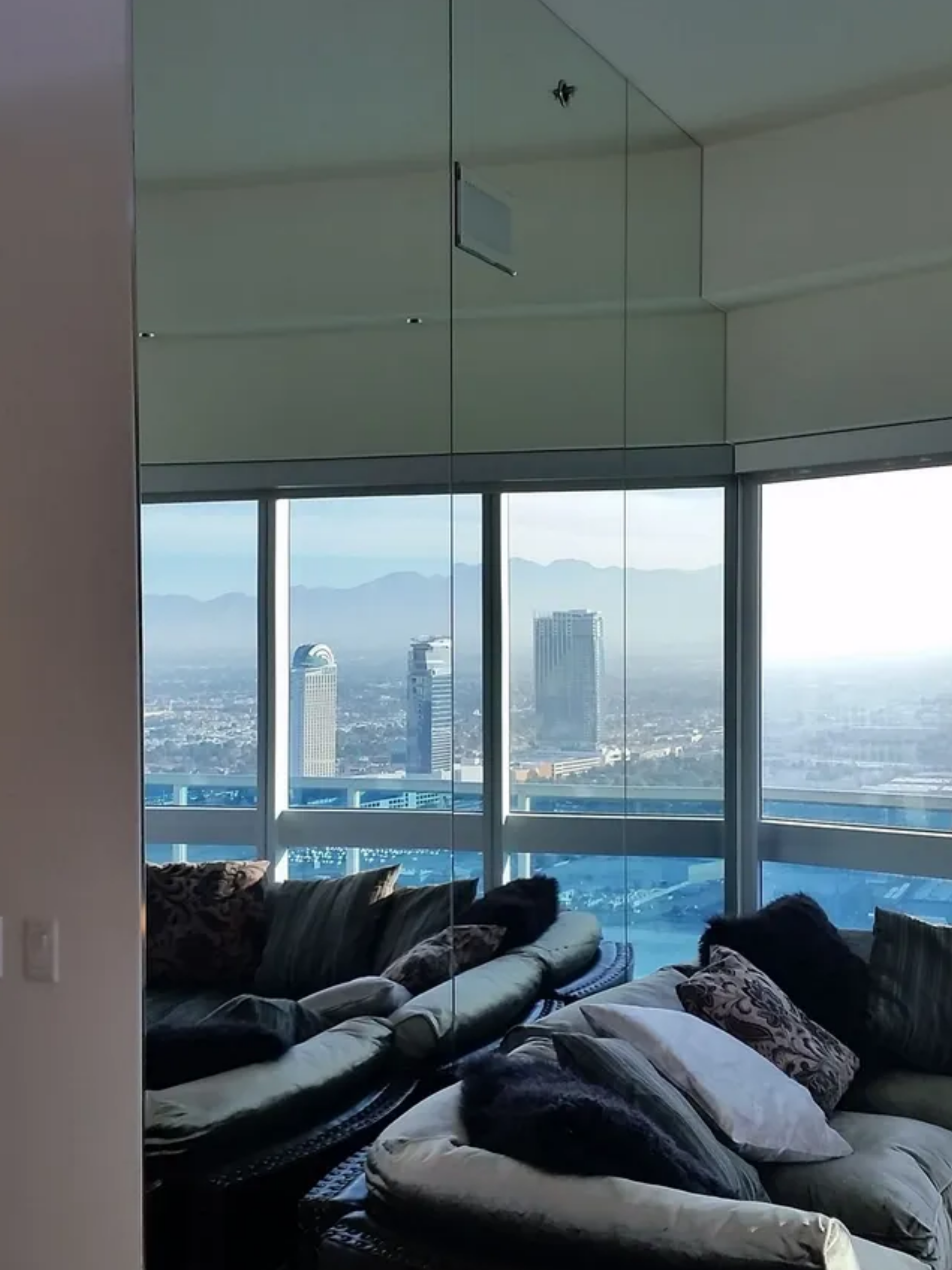 Modern living room with dark sofas and floor-to-ceiling windows overlooking a city skyline and mountains