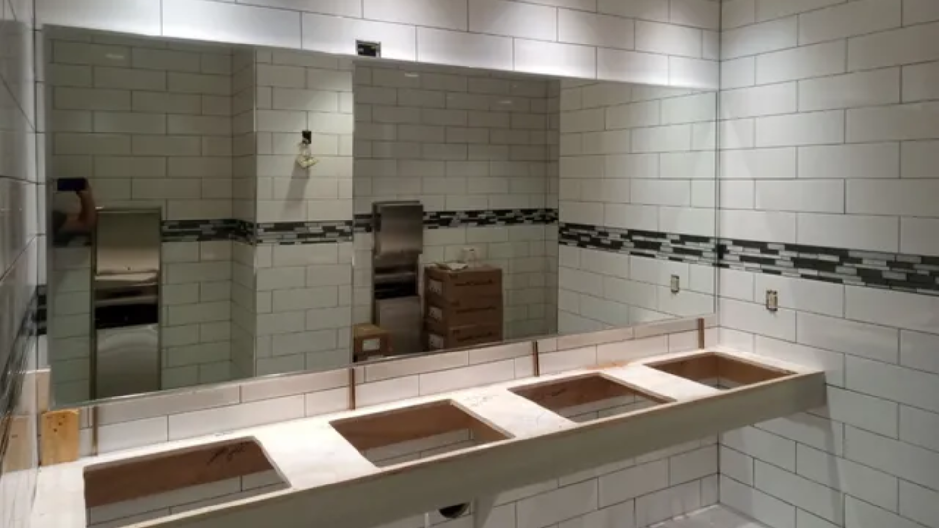 Public restroom with tiled walls, mirrors, and a long row of open sinks and counters