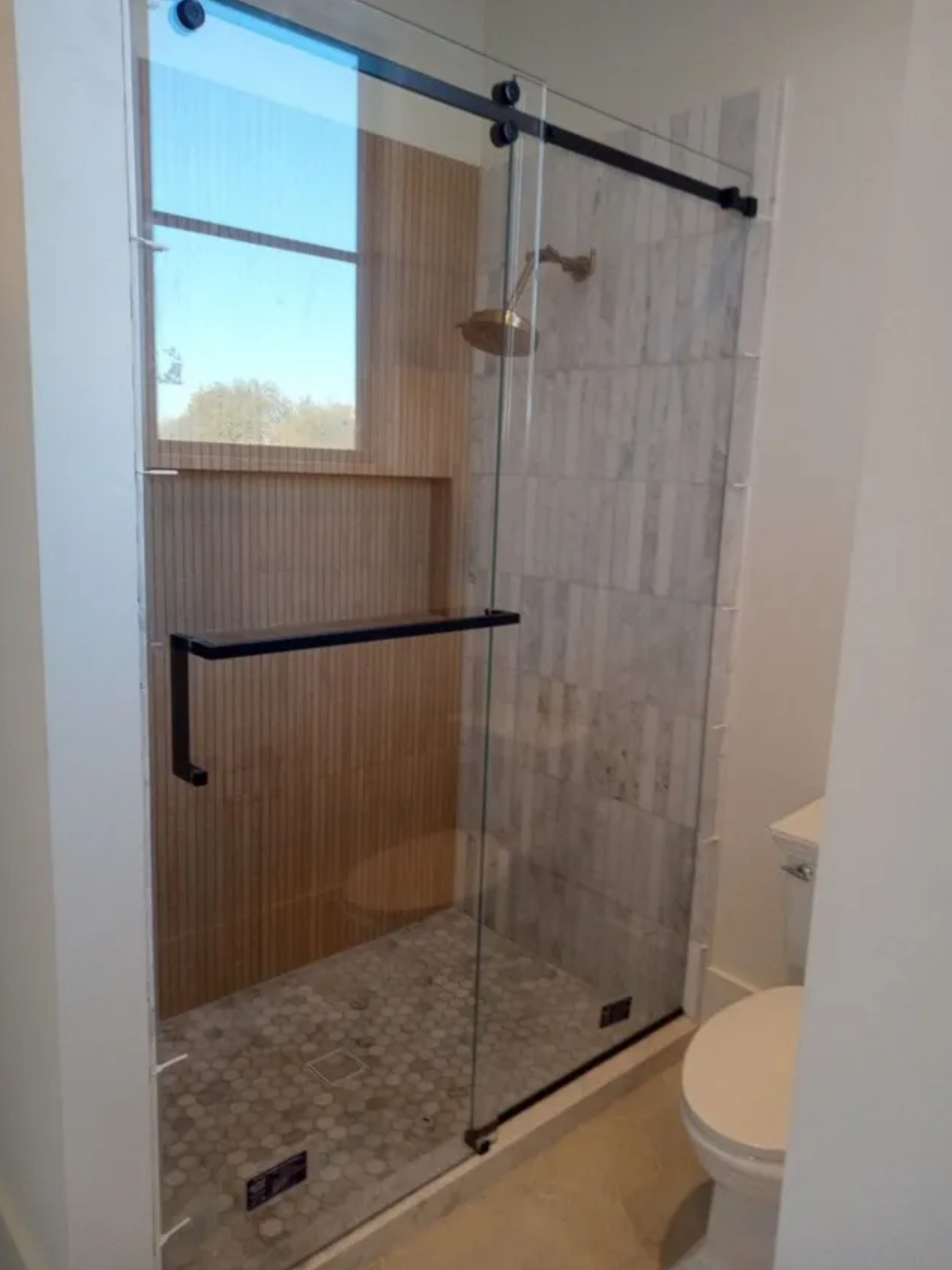 Glass walk-in shower with black hardware, built-in shelf, and a toilet beside it