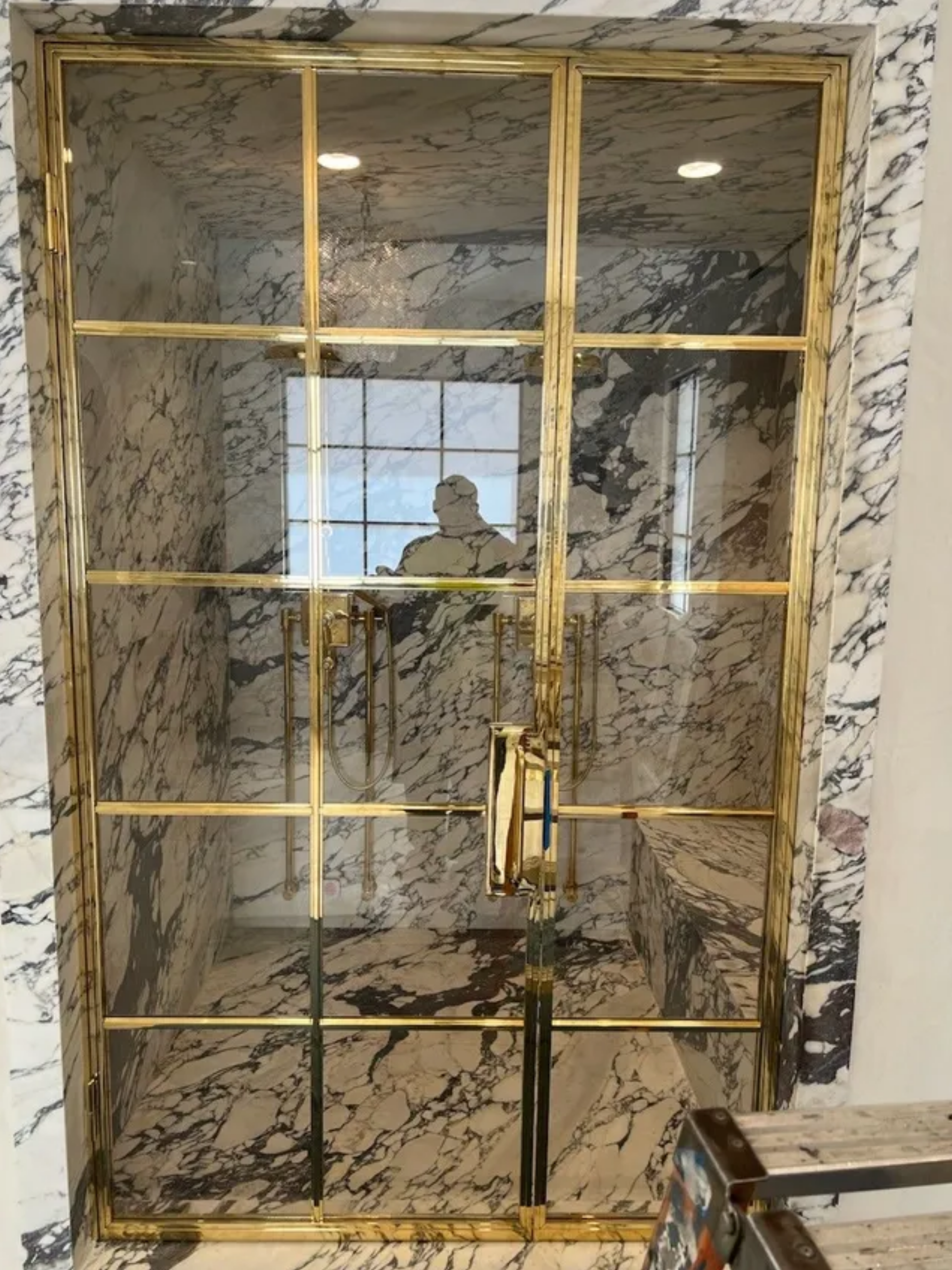 Marble-framed glass shower door with gold trim and handle in a bathroom