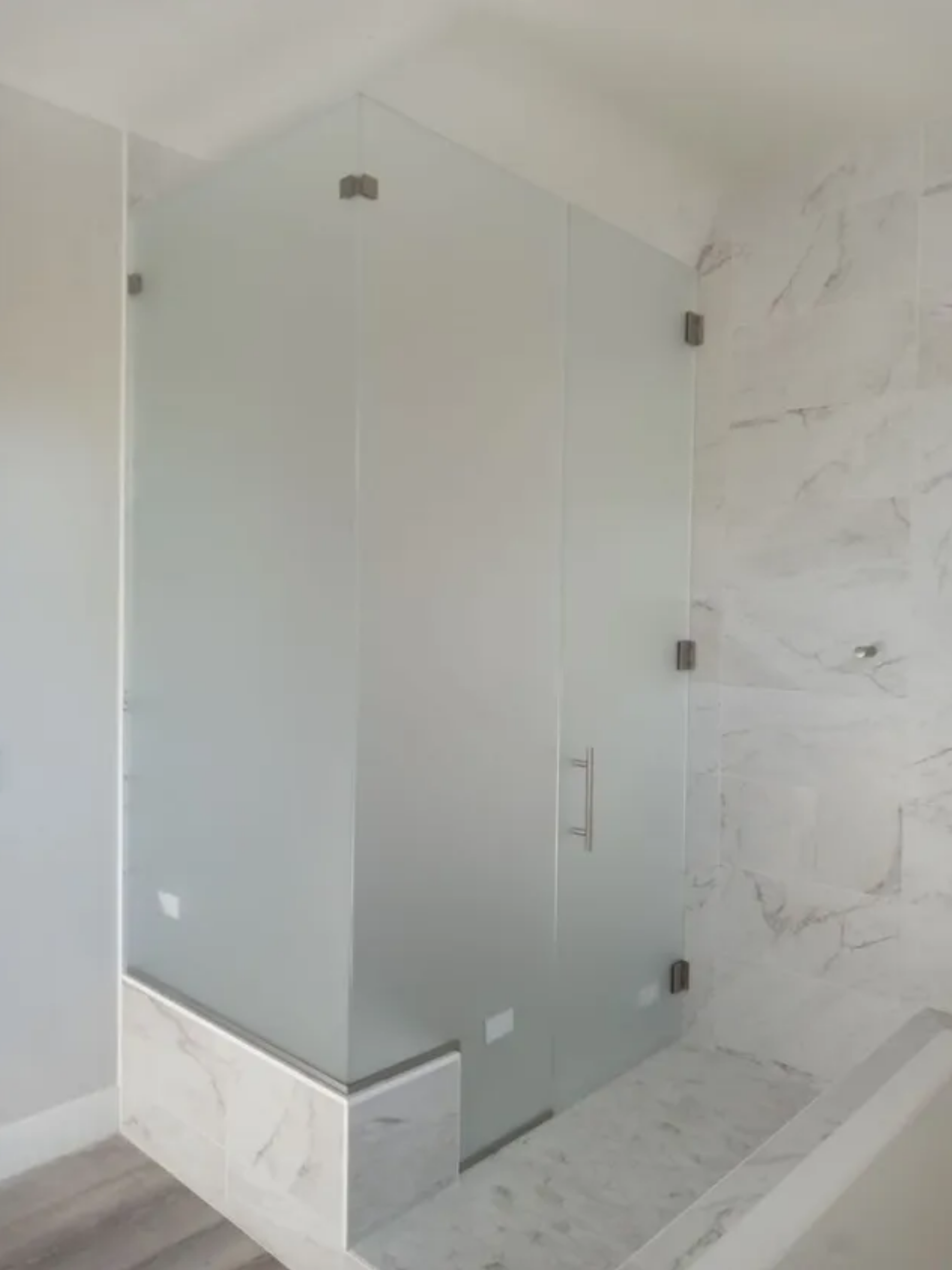 Frosted glass shower enclosure with marble-tile base and white bathroom walls