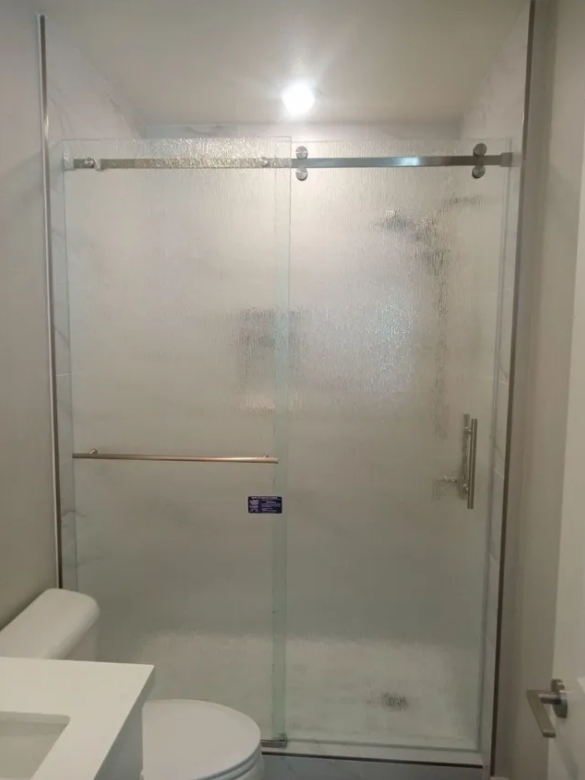 Frosted glass shower stall with sliding door in a small bathroom, next to a toilet and sink.