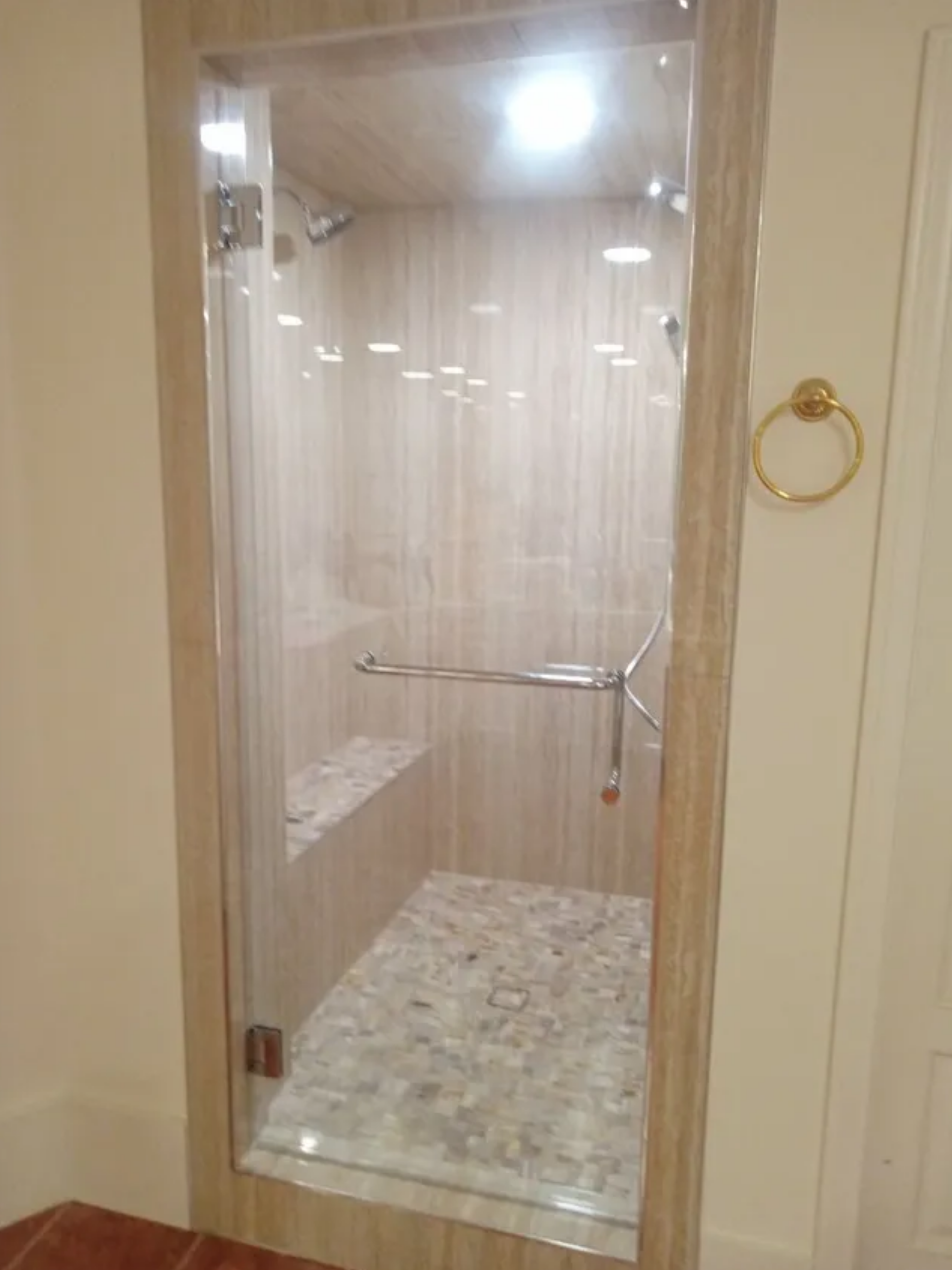 Glass shower enclosure with beige tile walls and a stone shower floor behind a doorway