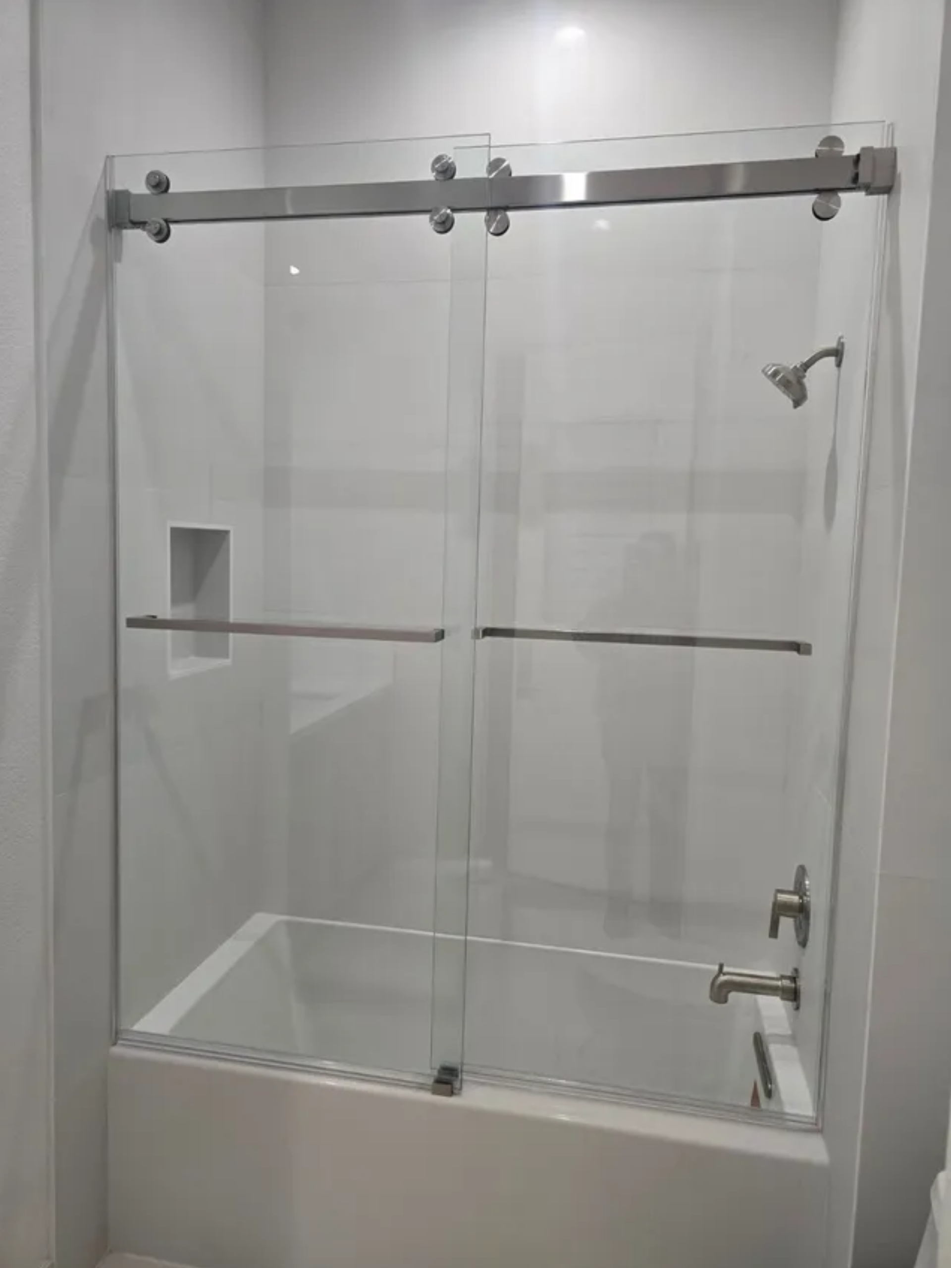 Glass shower stall with chrome fixtures and a built-in shelf in a tiled bathroom