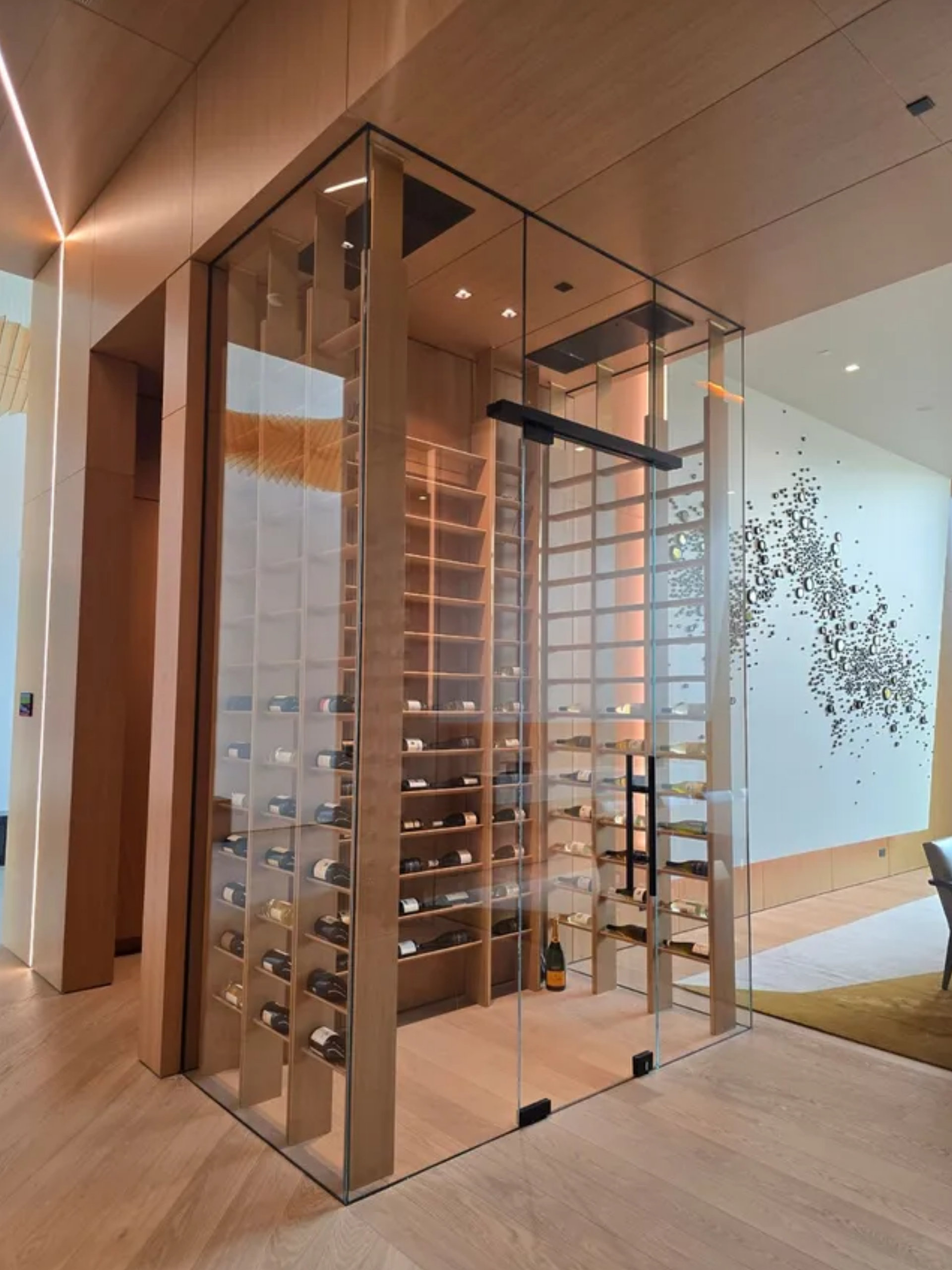 Glass wine display cellar in a modern hallway with warm wood accents