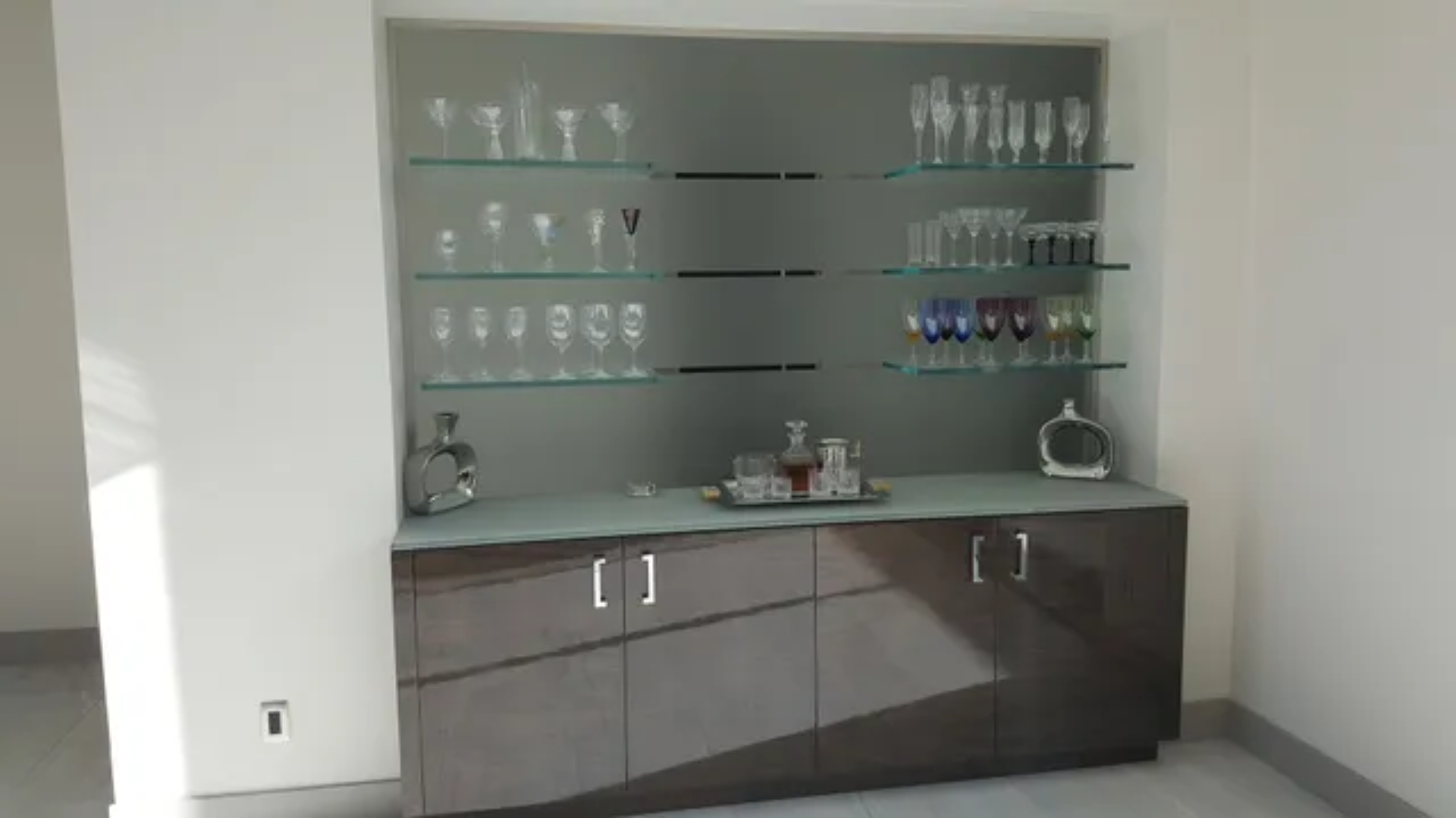 Modern glass shelf display with glassware and a countertop cabinet in a bright room