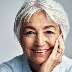 Smiling person with short silver hair resting their face on their hand