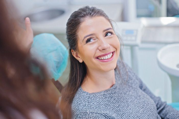 Smiling woman reclining in a dental chair while a dentist works nearby