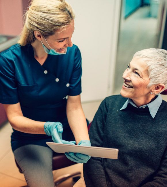 Caregiver in blue scrubs shows a clipboard to an elderly patient in a clinic room
