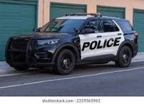 A black and white police car is parked on the side of the road in front of a garage. A black and white police car is parked on the side of the road in front of a garage.