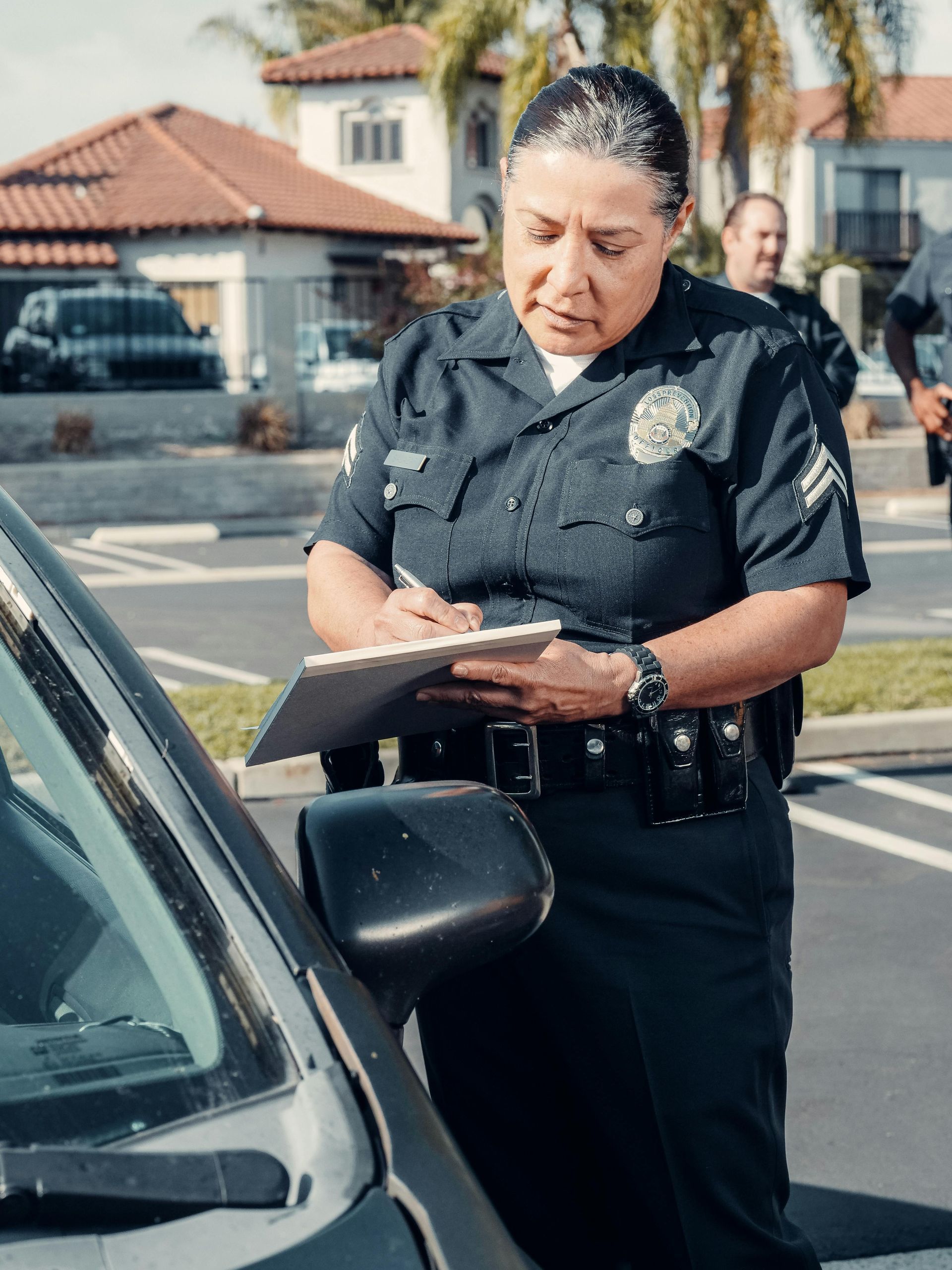 A police officer is writing on a clipboard next to a car.