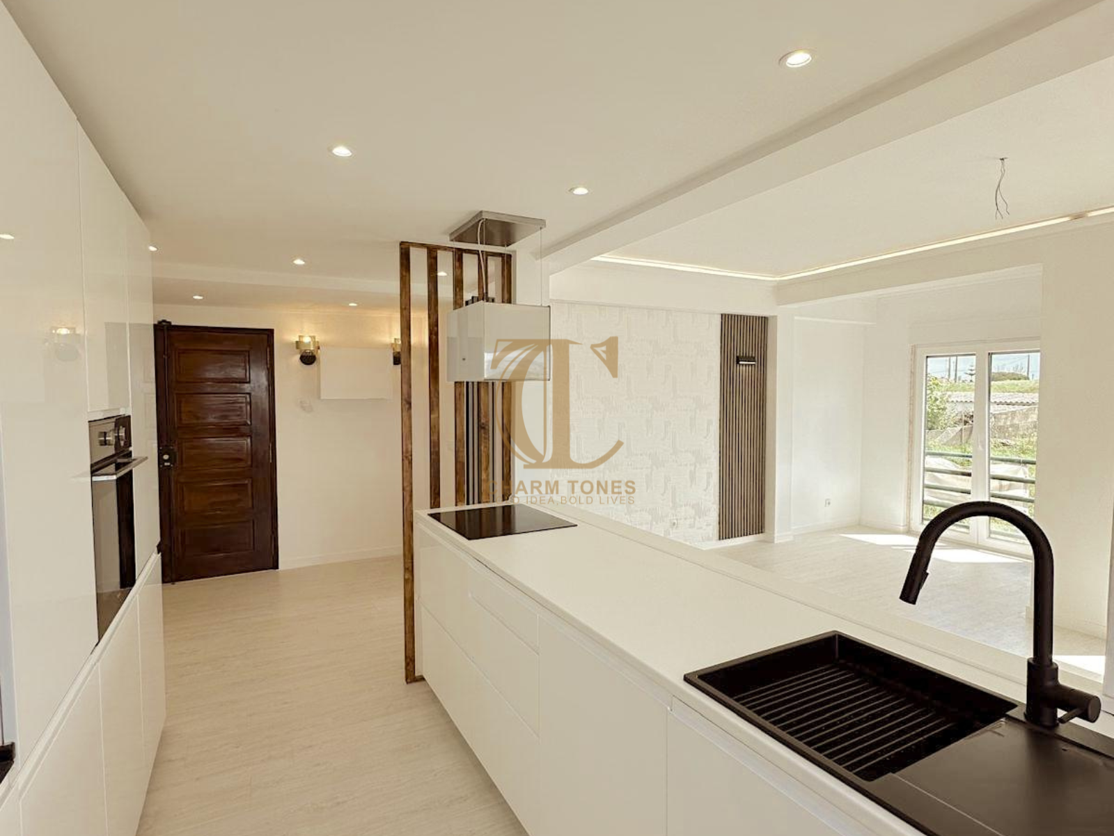 Cozinha moderna com armários brancos, ilha, pia preta e aberta para uma sala de estar.